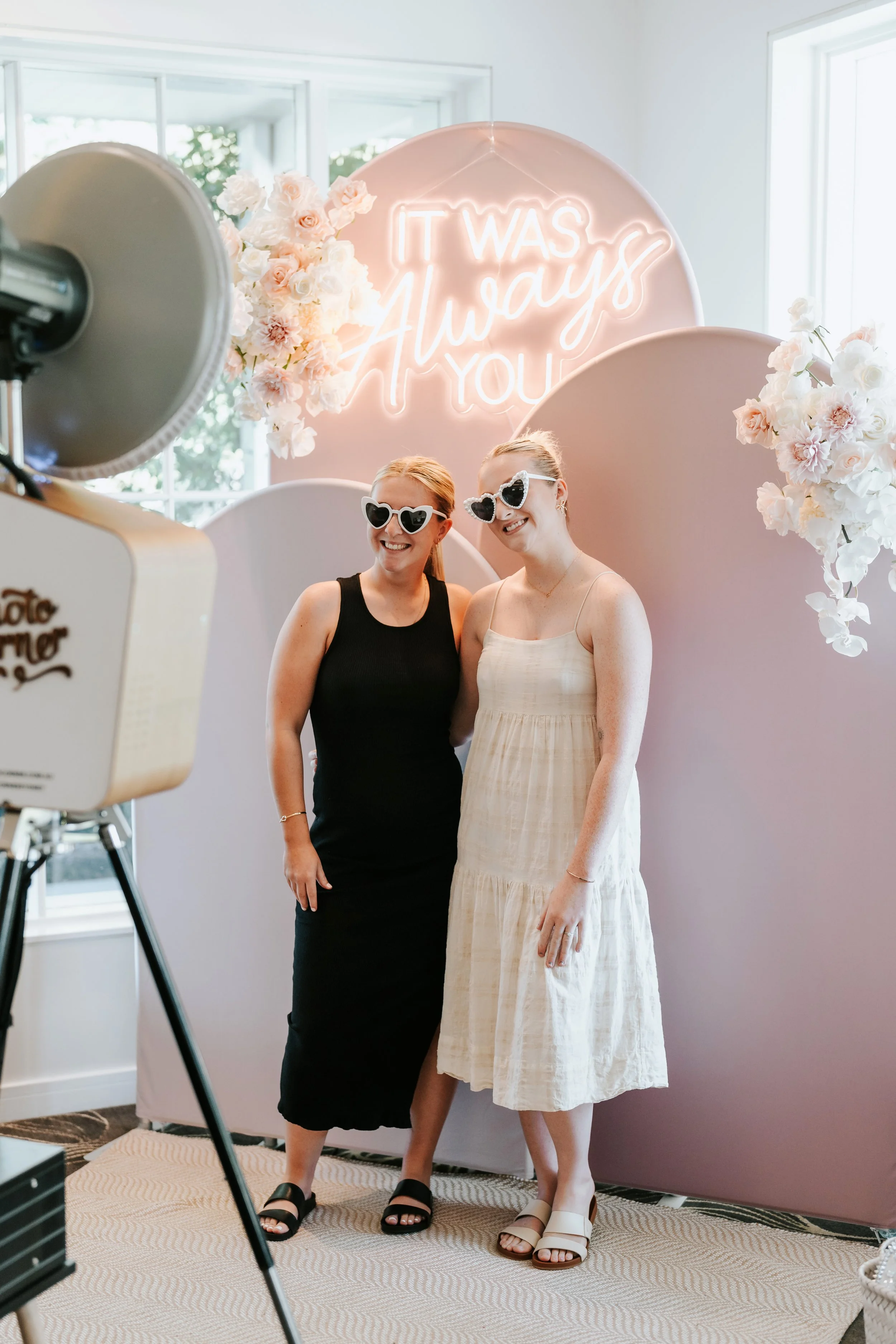 Photo Corner photo booth with Blush Horizon layered arch backdrop, neon sign and floral styling at a wedding venue.