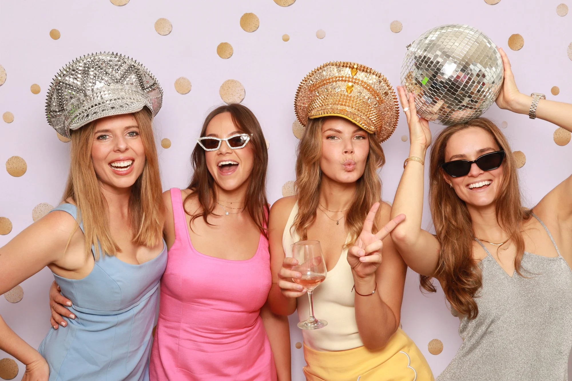 Wedding guests wearing statement hats and posing with a disco ball in a Photo Corner photo booth.