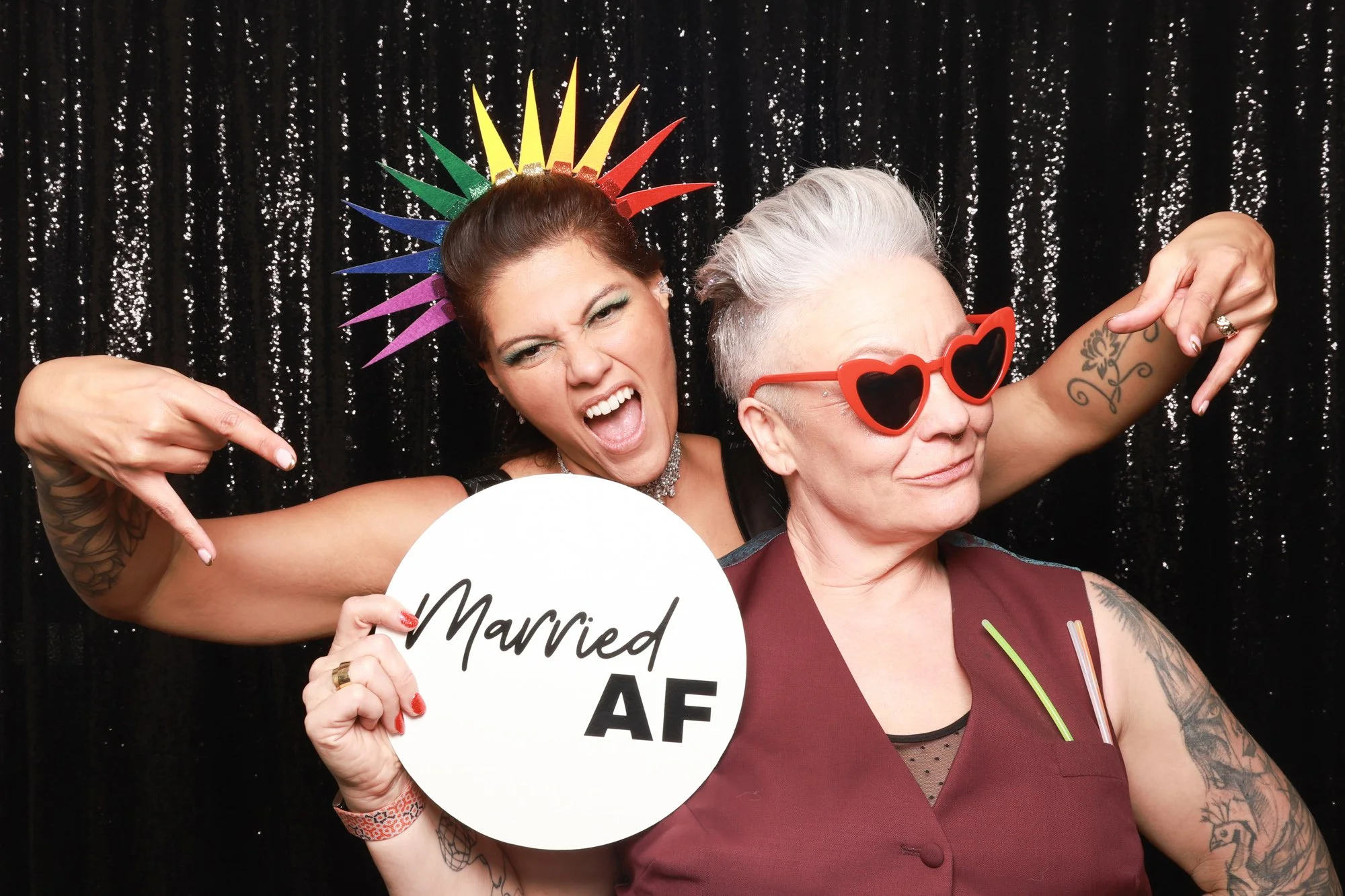 Same-sex couple celebrating their wedding with stylish photo booth props and personalised signage.