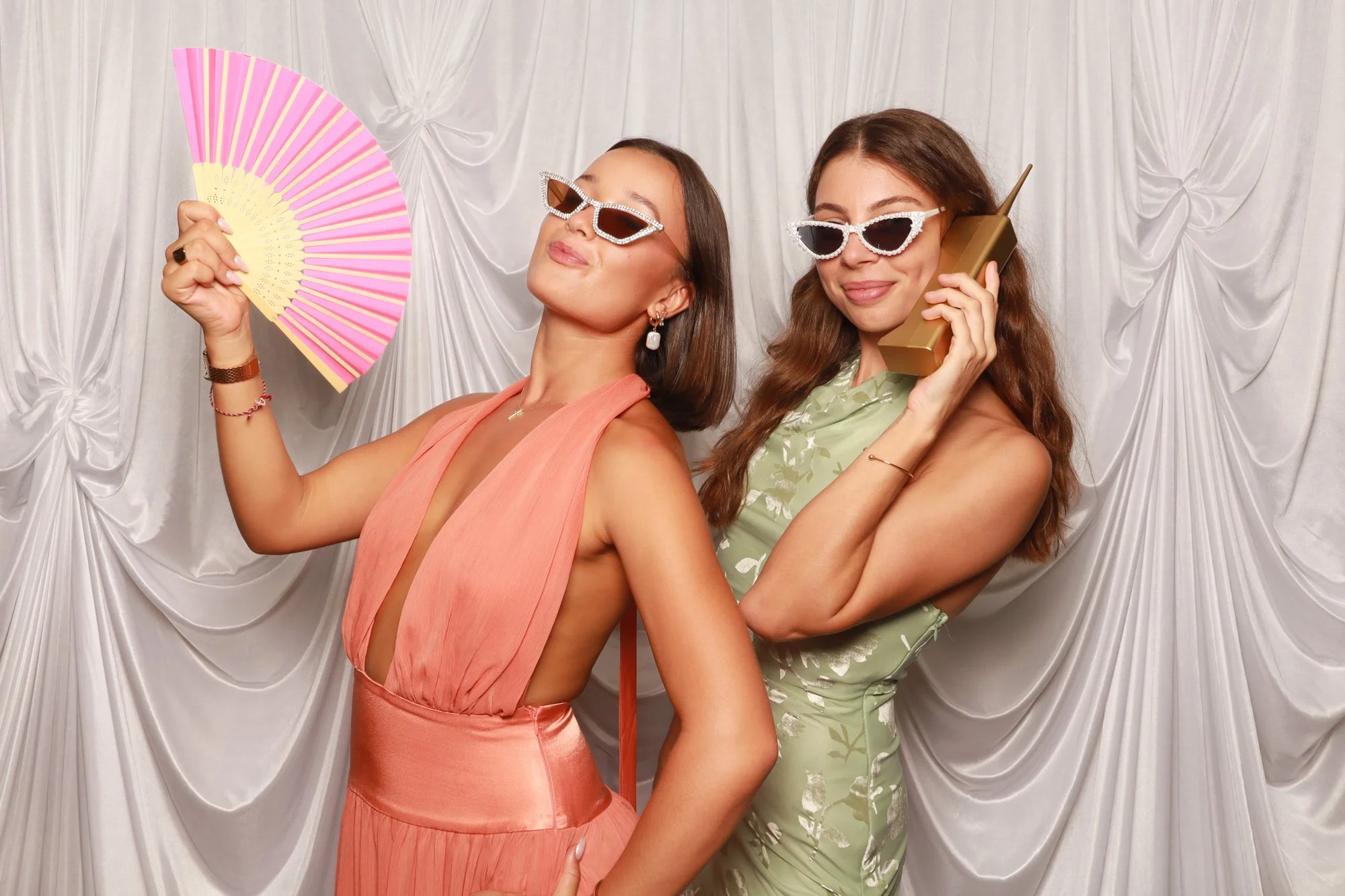 Wedding guests posing with hand fans and a retro phone in front of a drapery backdrop.