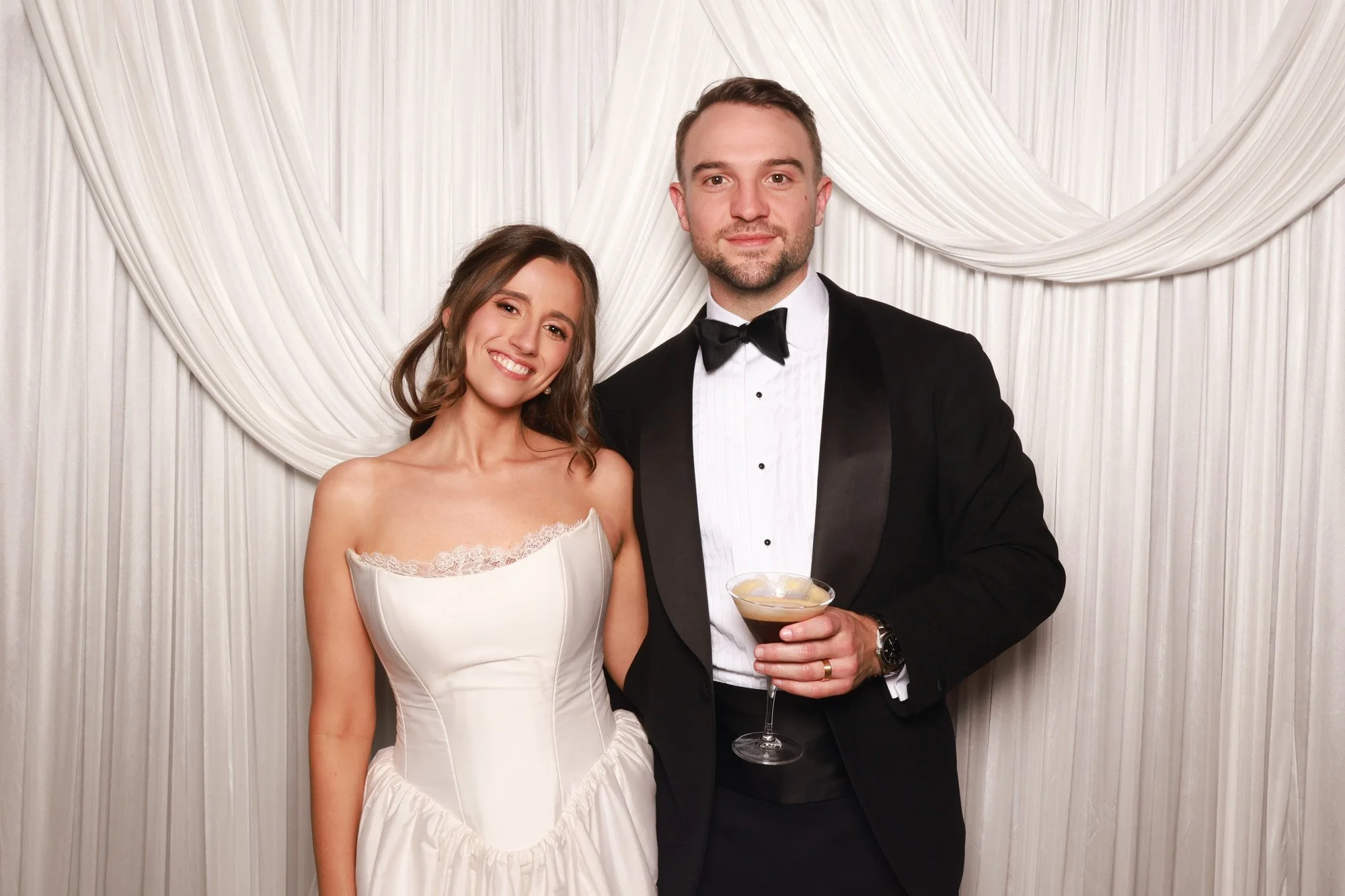 Wedding guests posing against the soft layered ivory draping of the Cloud Whisper photo booth backdrop.