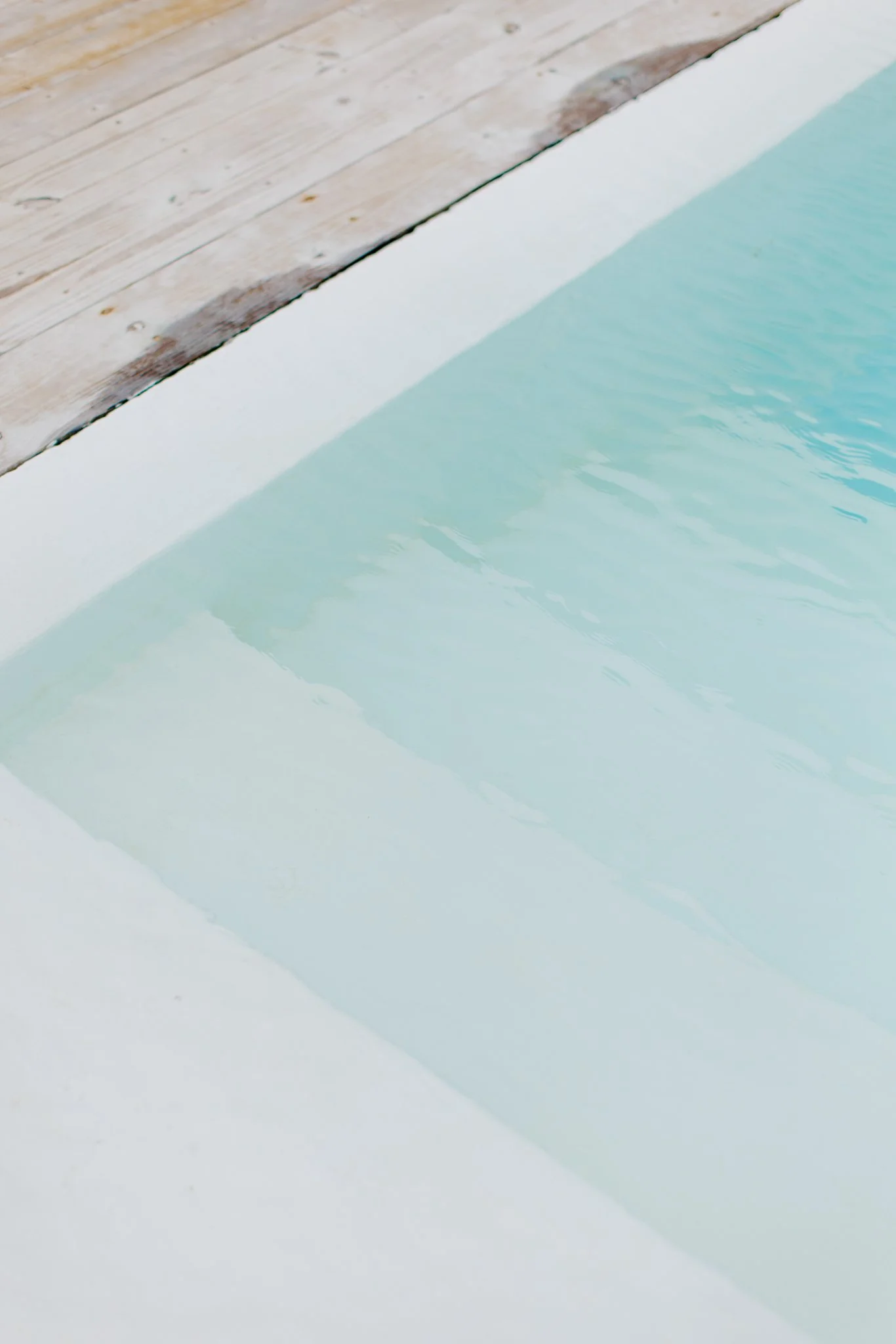 Close-up of a swimming pool with light blue water and a wooden deck surface nearby.