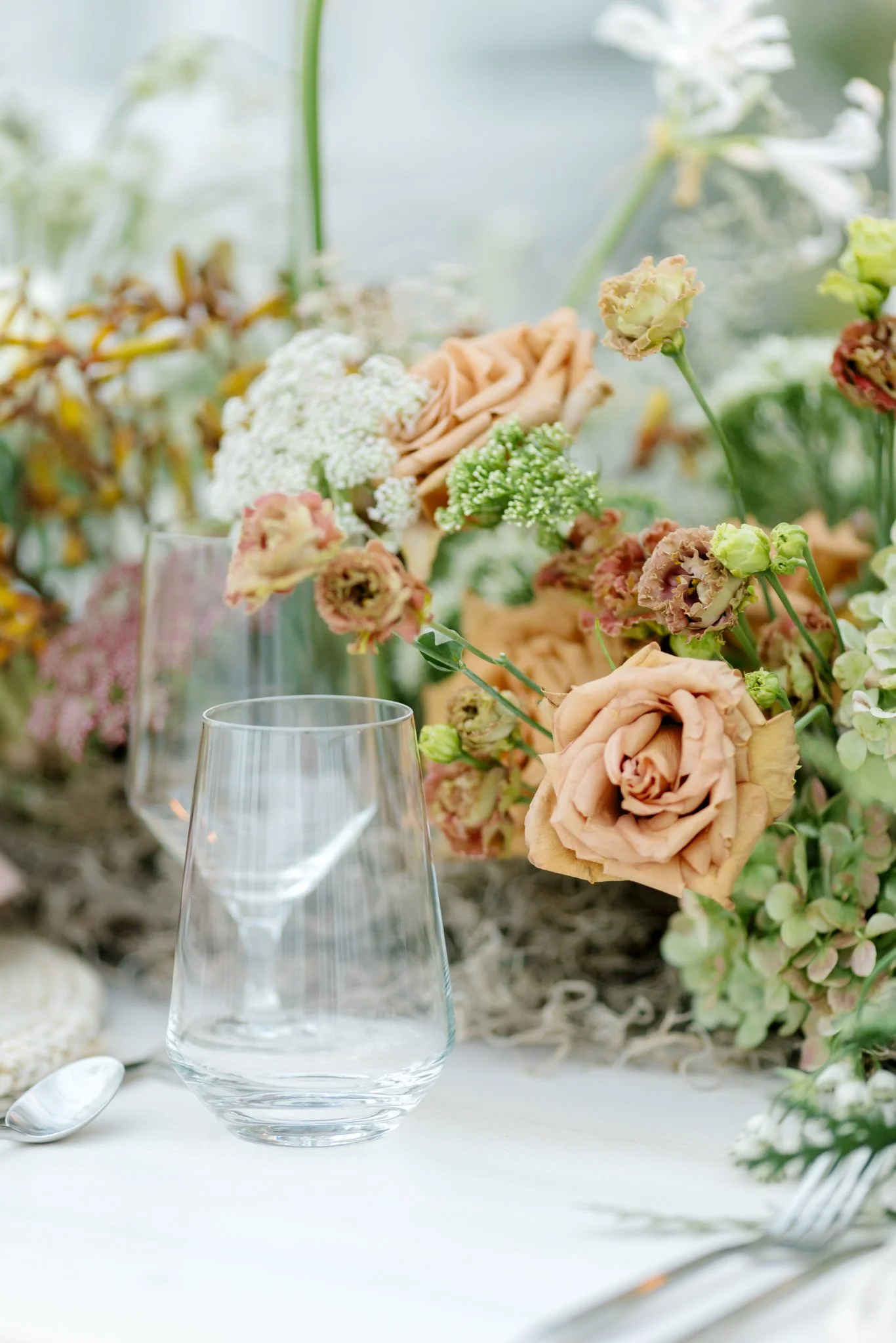 Empty glass on a table with floral centerpiece of pink and white flowers in a natural setting at Greenhouse on Harvard near Spokane, Washington.