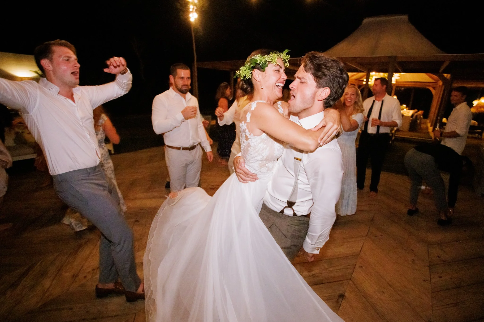 Bride and groom dancing at their wedding reception, surrounded by guests, with one guest dancing energetically in the background.