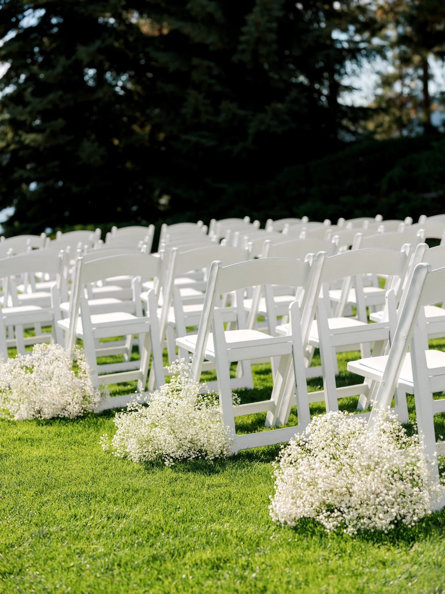 Rows of white ceremony chairs lined with clusters of baby’s breath on a green lawn at the Hagadone Event Center.
