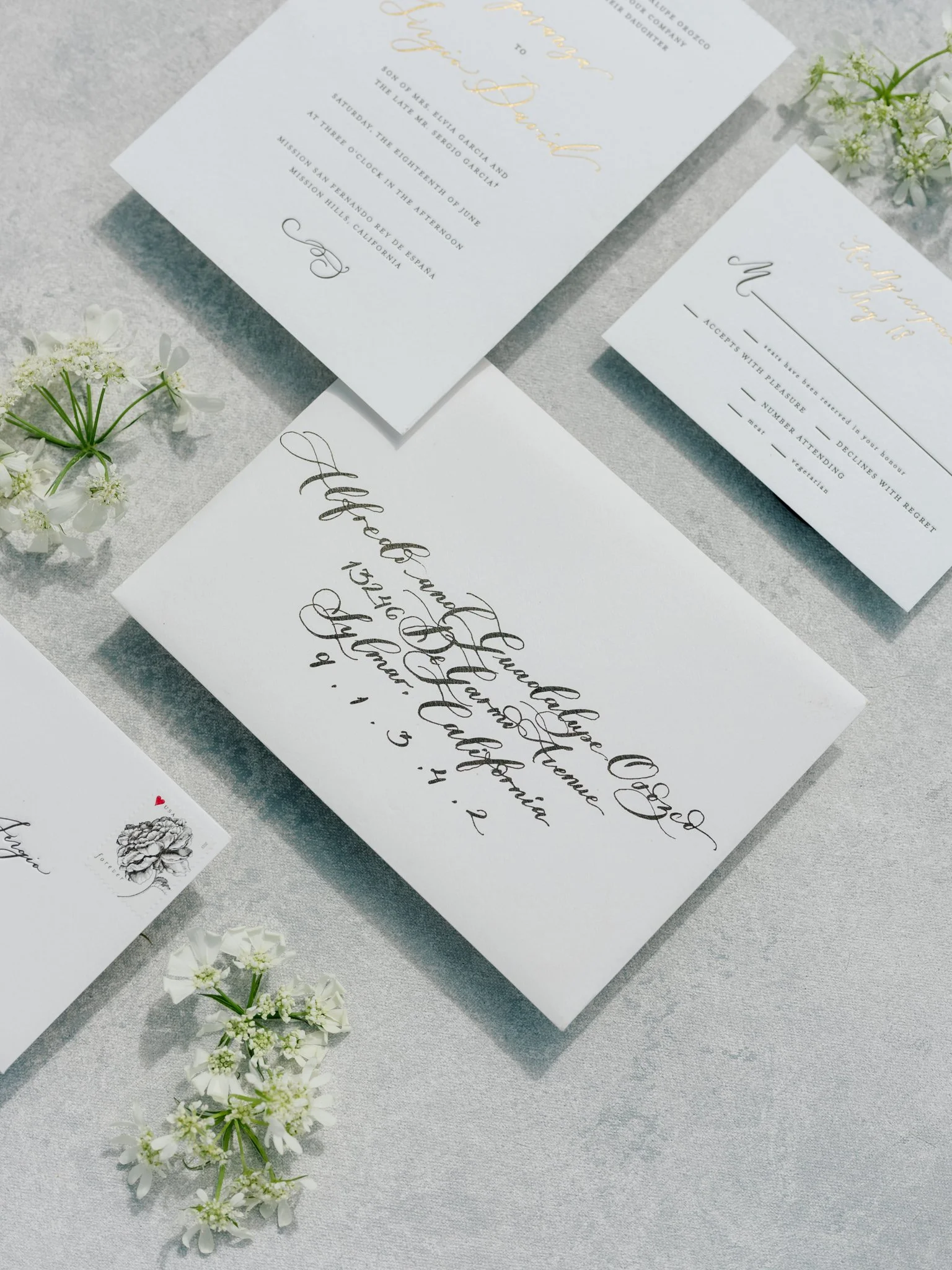 Wedding invitations and RSVP cards on a light gray surface, surrounded by white flowers at Greenhouse on Harvard near Spokane, Washington.