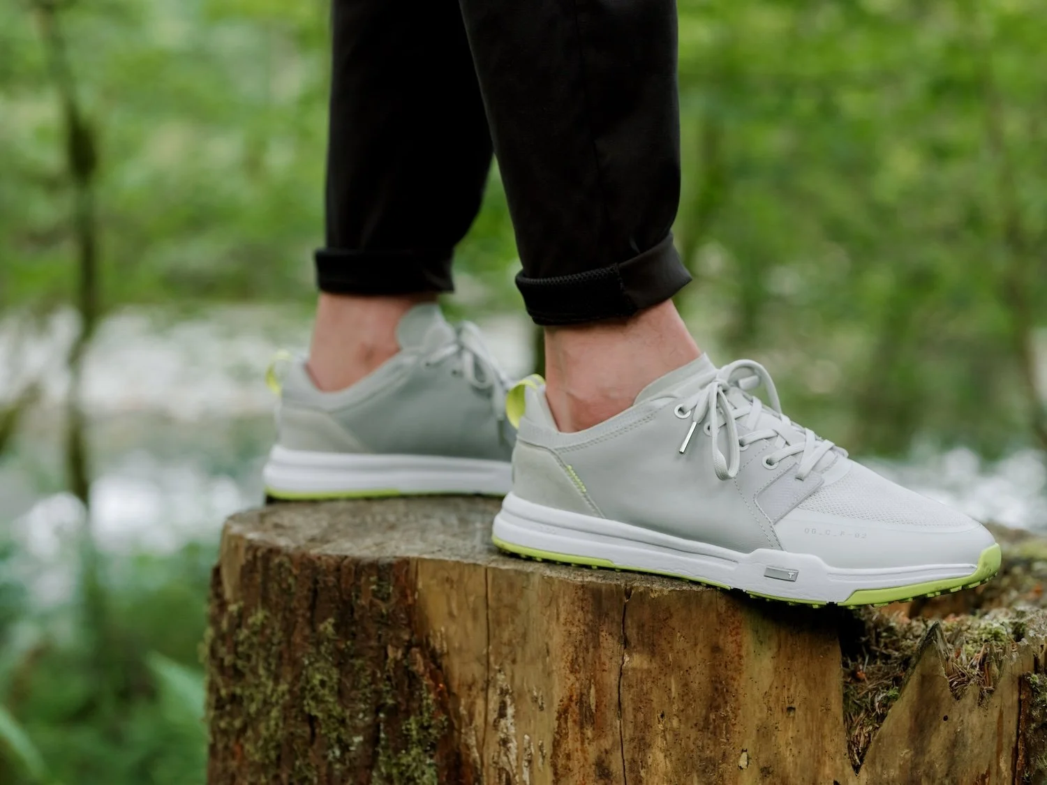 Person wearing white sneakers standing on a tree stump in a forested area.