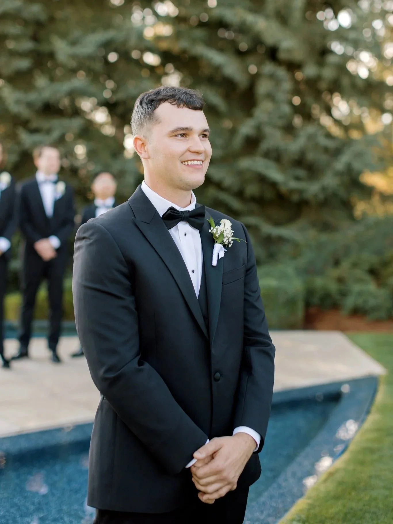 Groom smiling as he waits at the altar with groomsmen behind him during an outdoor wedding ceremony at the Hagadone Event Center.