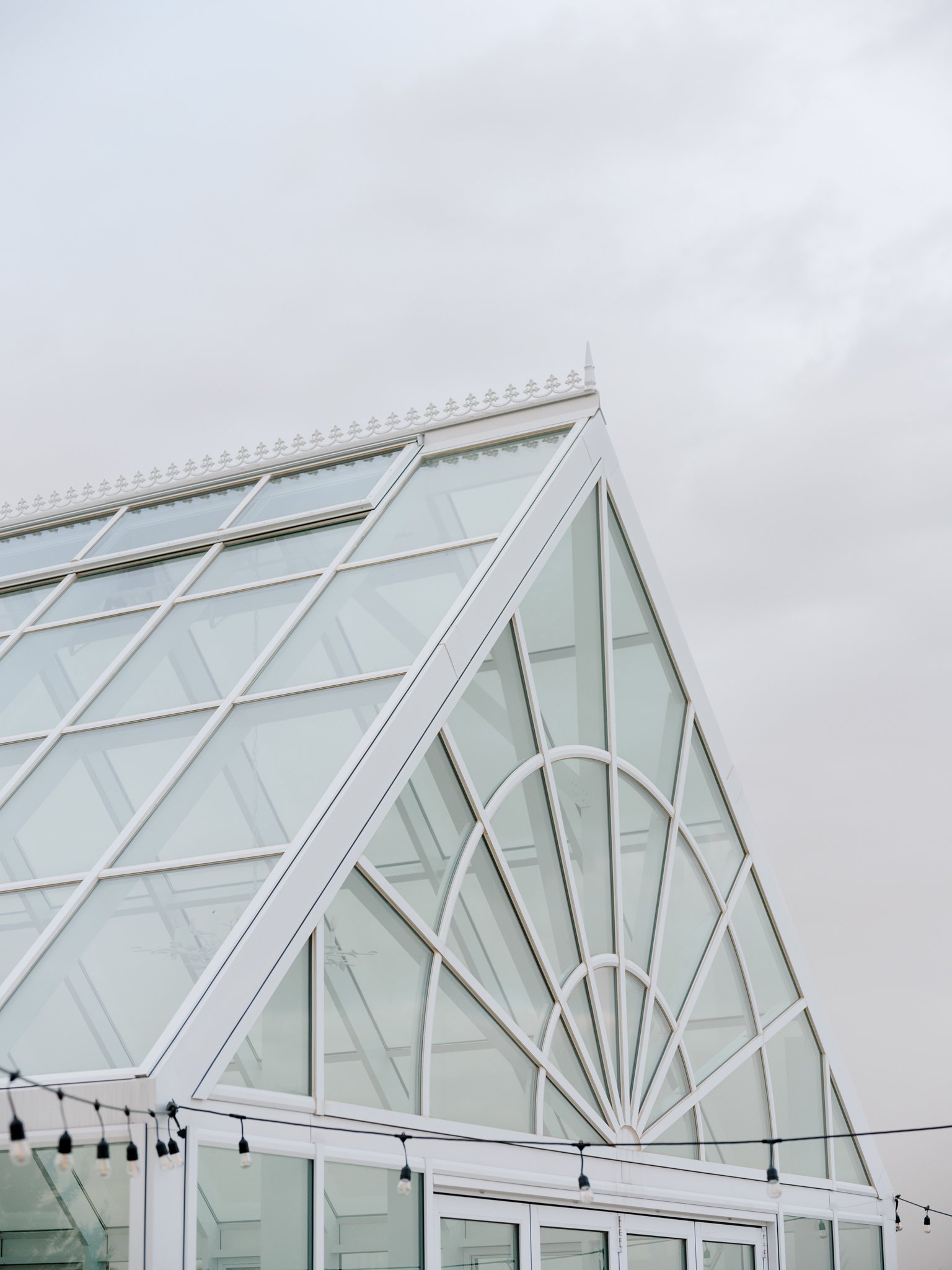 Close-up view of a modern glass greenhouse or conservatory with geometric design and a pointed roof, with string lights hanging in front at Greenhouse on Harvard near Spokane, Washington.