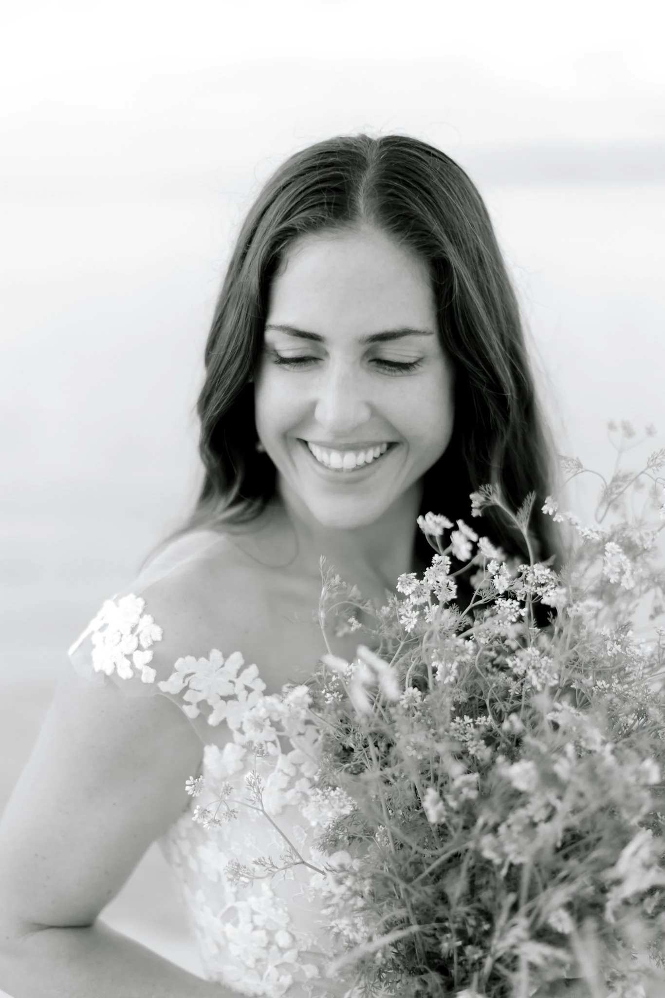 Black and white photo of a smiling woman with long wavy hair holding a bouquet of flowers.