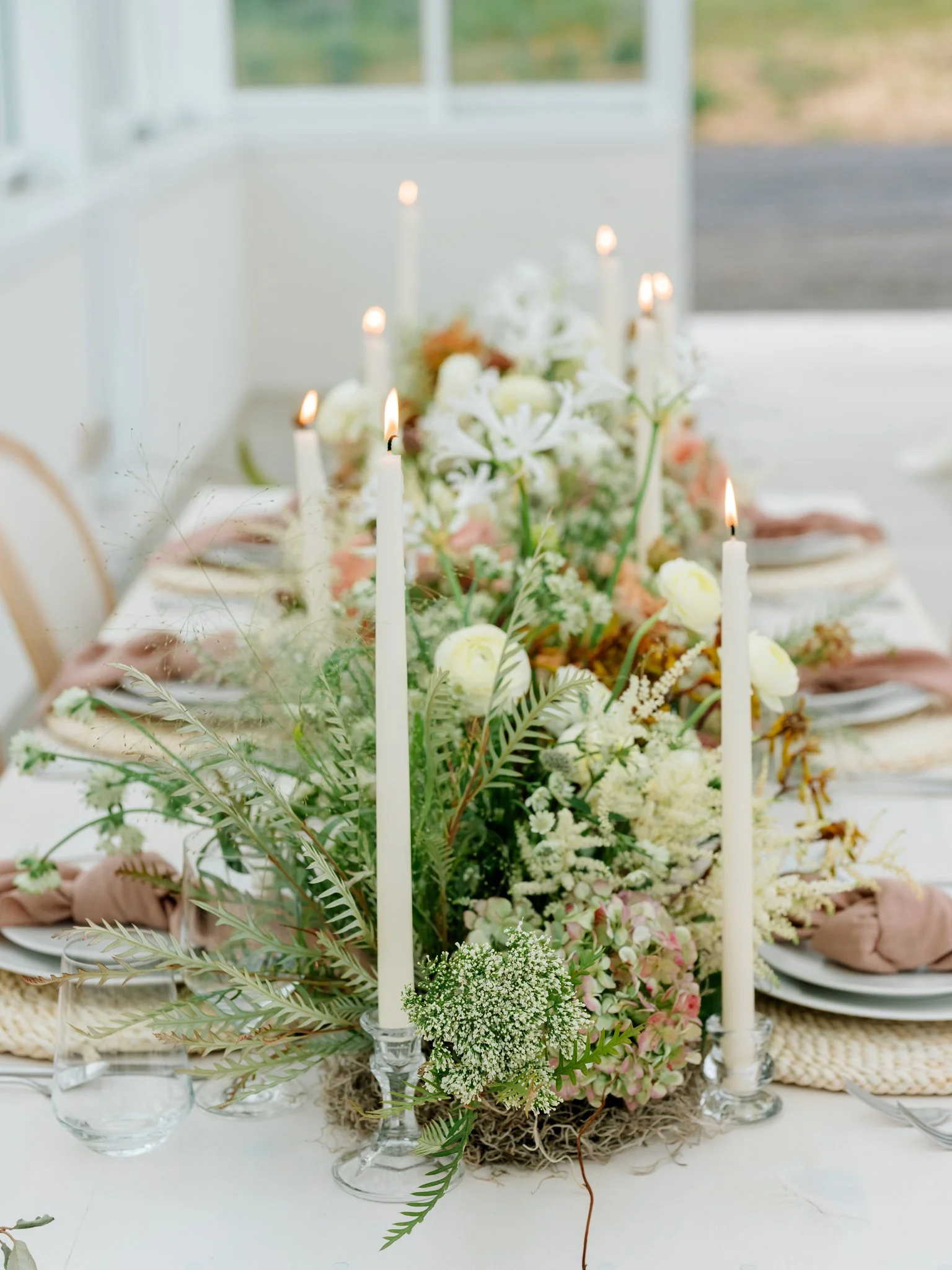 A decorated dining table with white candles and a floral centerpiece featuring white and pink flowers, greenery, and candles at Greenhouse on Harvard near Spokane, Washington.
