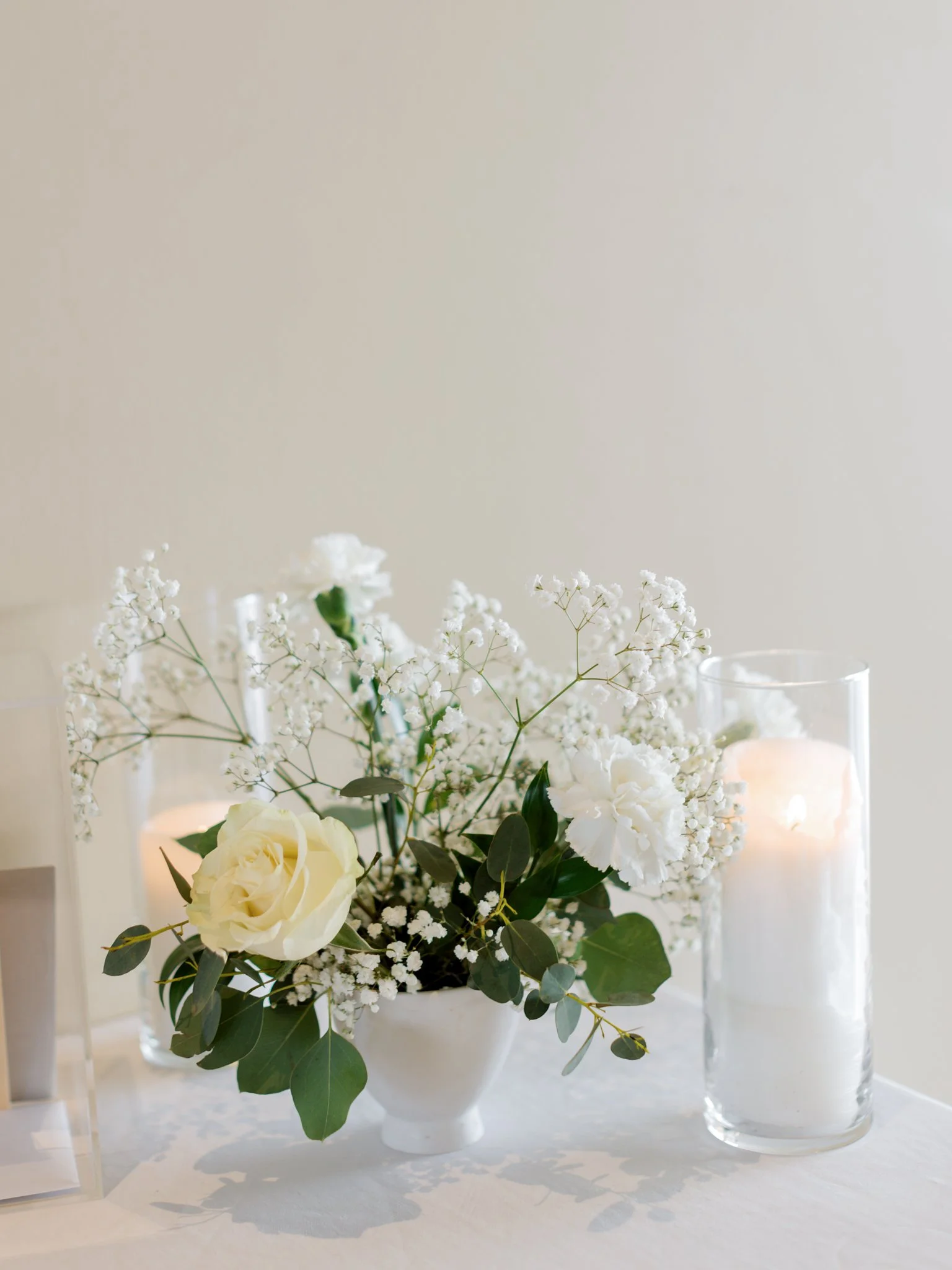 White flower arrangement with roses and baby's breath in a white vase, beside a tall glass candle holder with a lit candle at the Hagadone Event Center in Coeur d'Alene, Idaho.