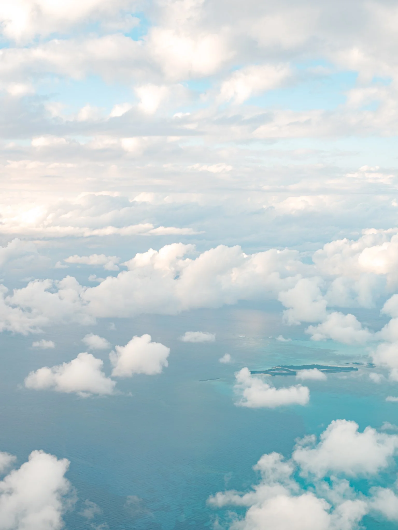 View of clouds over the ocean taken from high altitude, with some land visible in the distance.