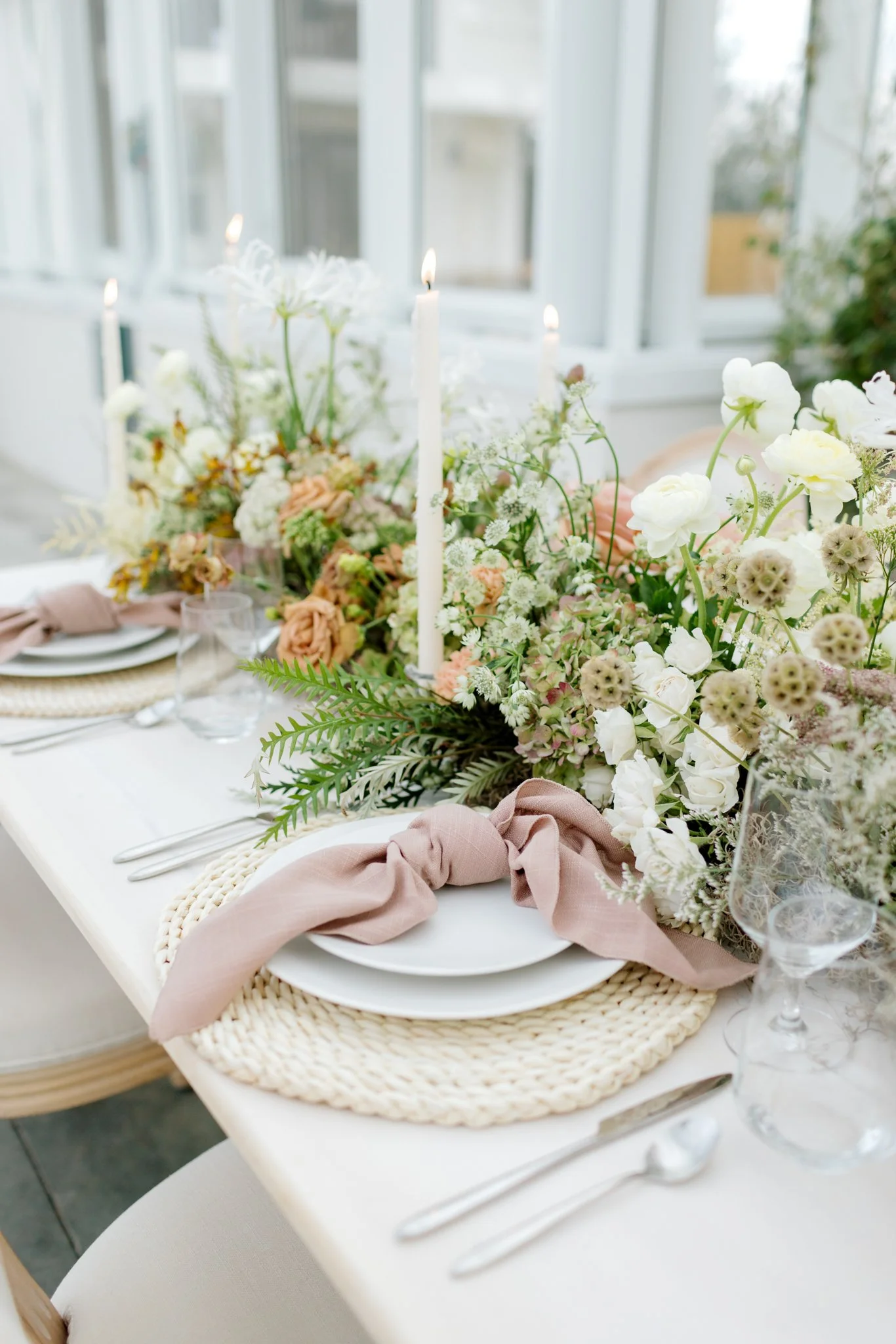 Elegant dining table decorated with a lush floral centerpiece, pink napkins, and candles in a bright sunlit room at Greenhouse on Harvard near Spokane, Washington