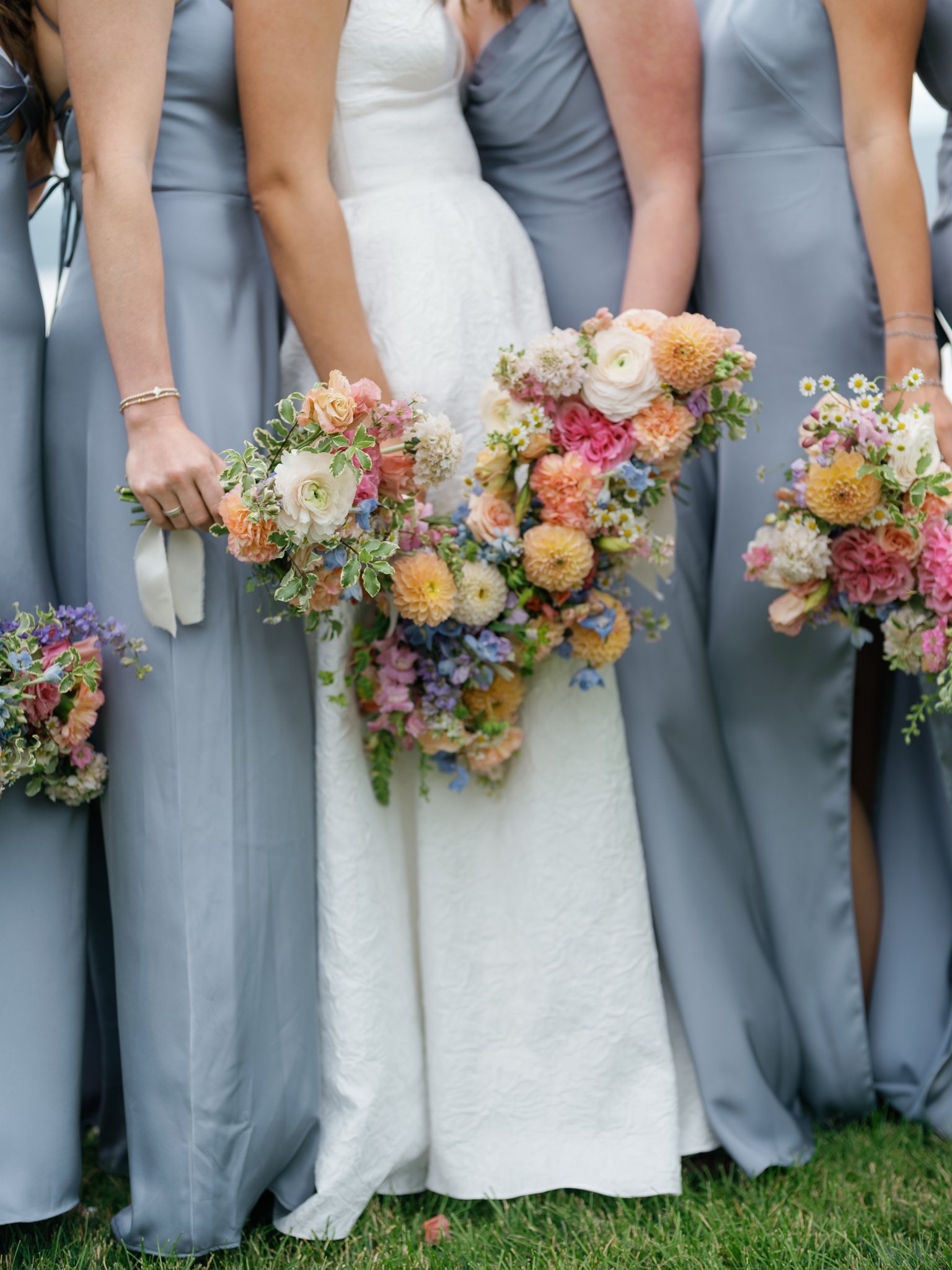 Wedding party holding bouquets, mainly a bride in a white dress and bridesmaids in gray dresses, with colorful flower arrangements  at Elk Point wedding in Coeur d’Alene.