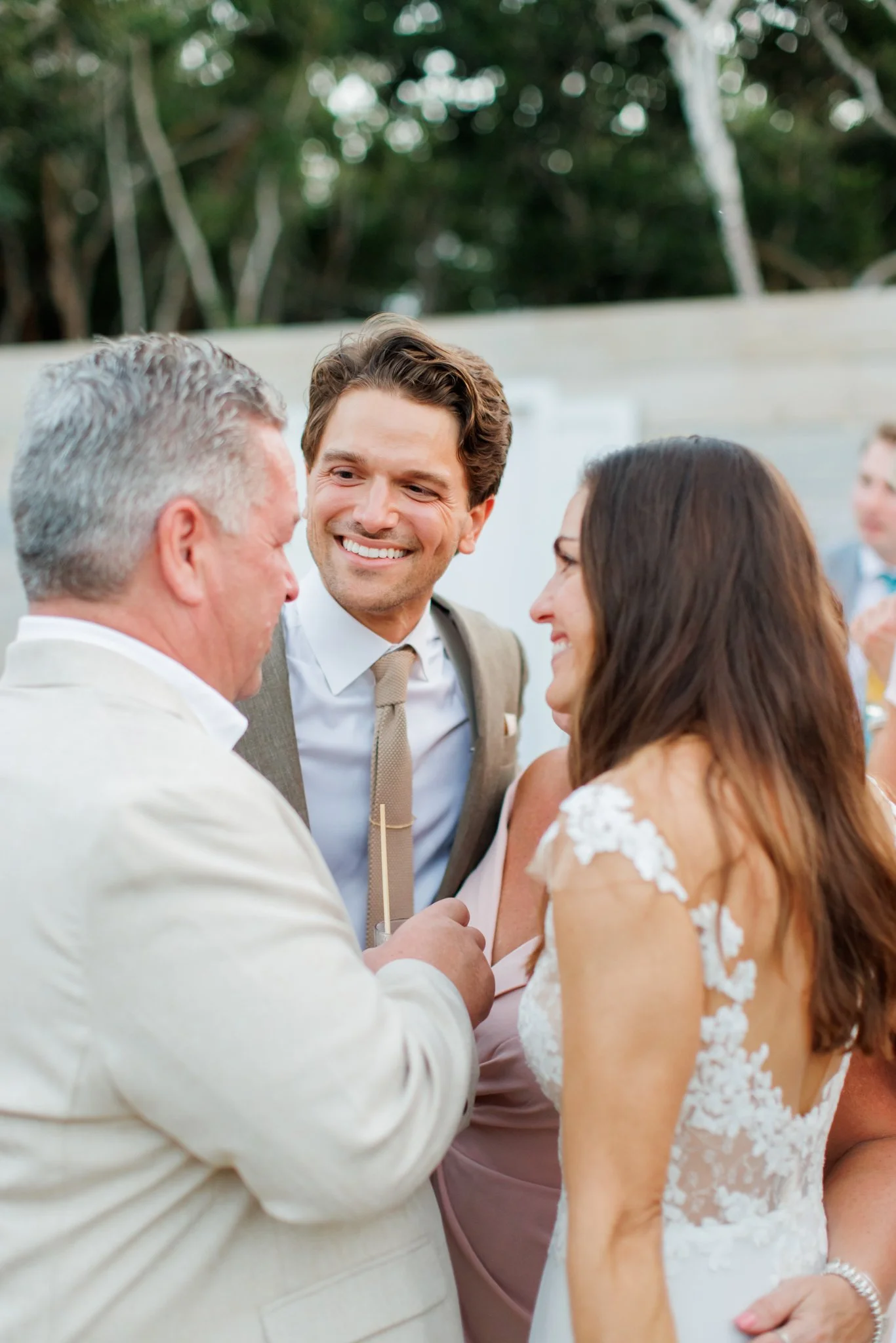 A happy couple and an older man at a wedding celebration, sharing a joyful moment outdoors.