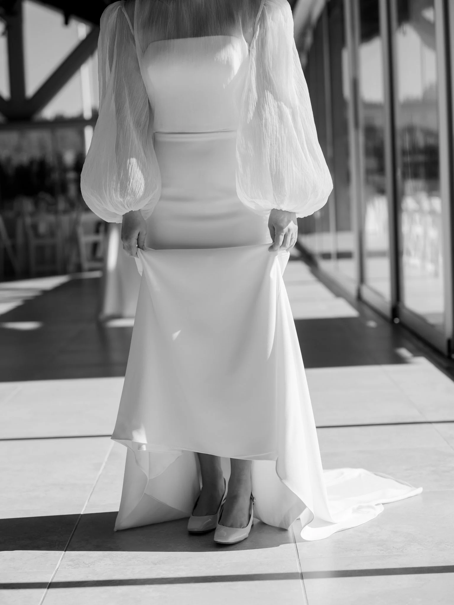 Bride in a wedding dress with puffed sheer sleeves and high heels, standing indoors near large glass windows at the Hagadone Event Center in Coeur d'Alene, Idaho.