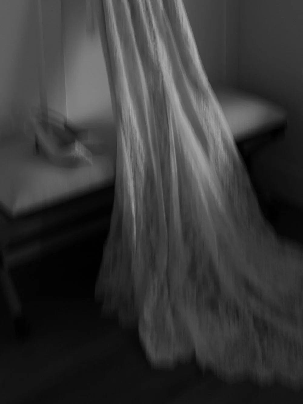 A wedding dress hanging on a bed in a hotel room with a phone on the bed.