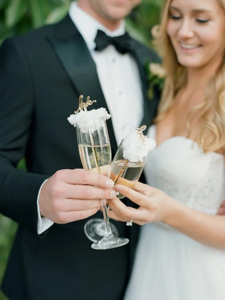 A bride and groom holding champagne glasses with festive stir sticks and whipped cream, celebrating their wedding.