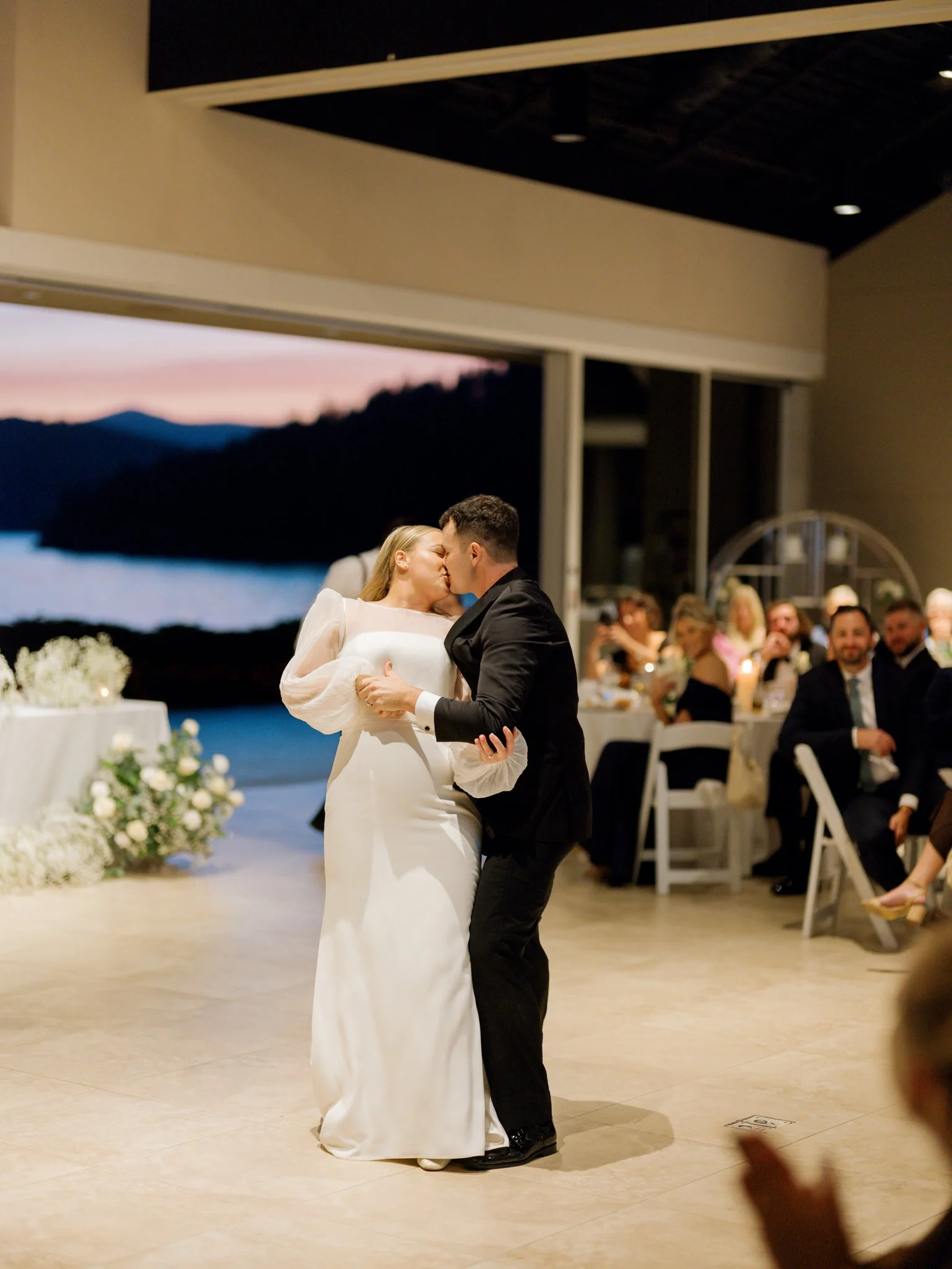 Couple sharing a kiss during their wedding dance at an indoor reception hall, with guests watching in the background at the Hagadone Event Center in Coeur d'Alene, Idaho.