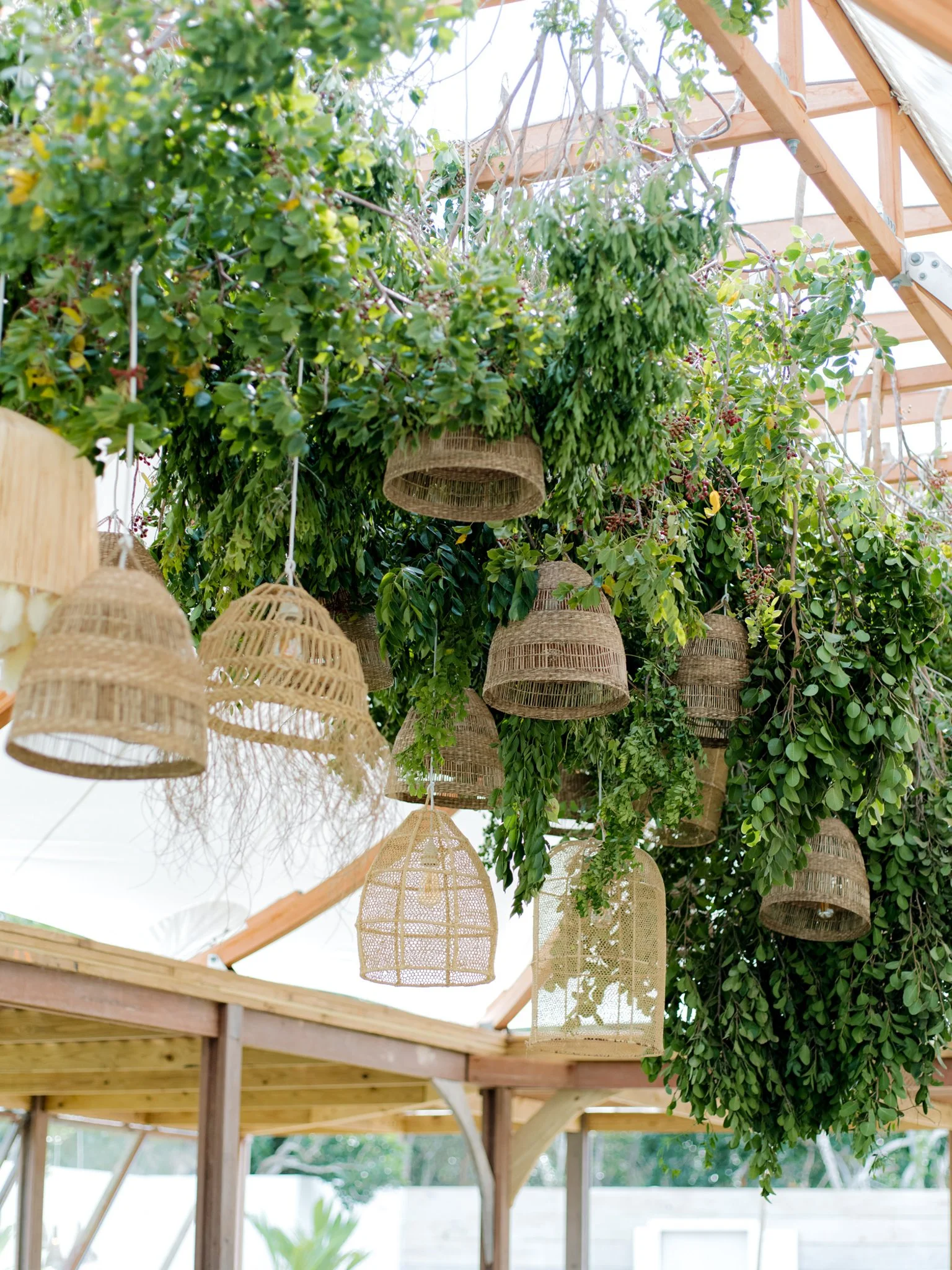 Hanging wicker and rattan lamps surrounded by lush green foliage under a wooden structure.