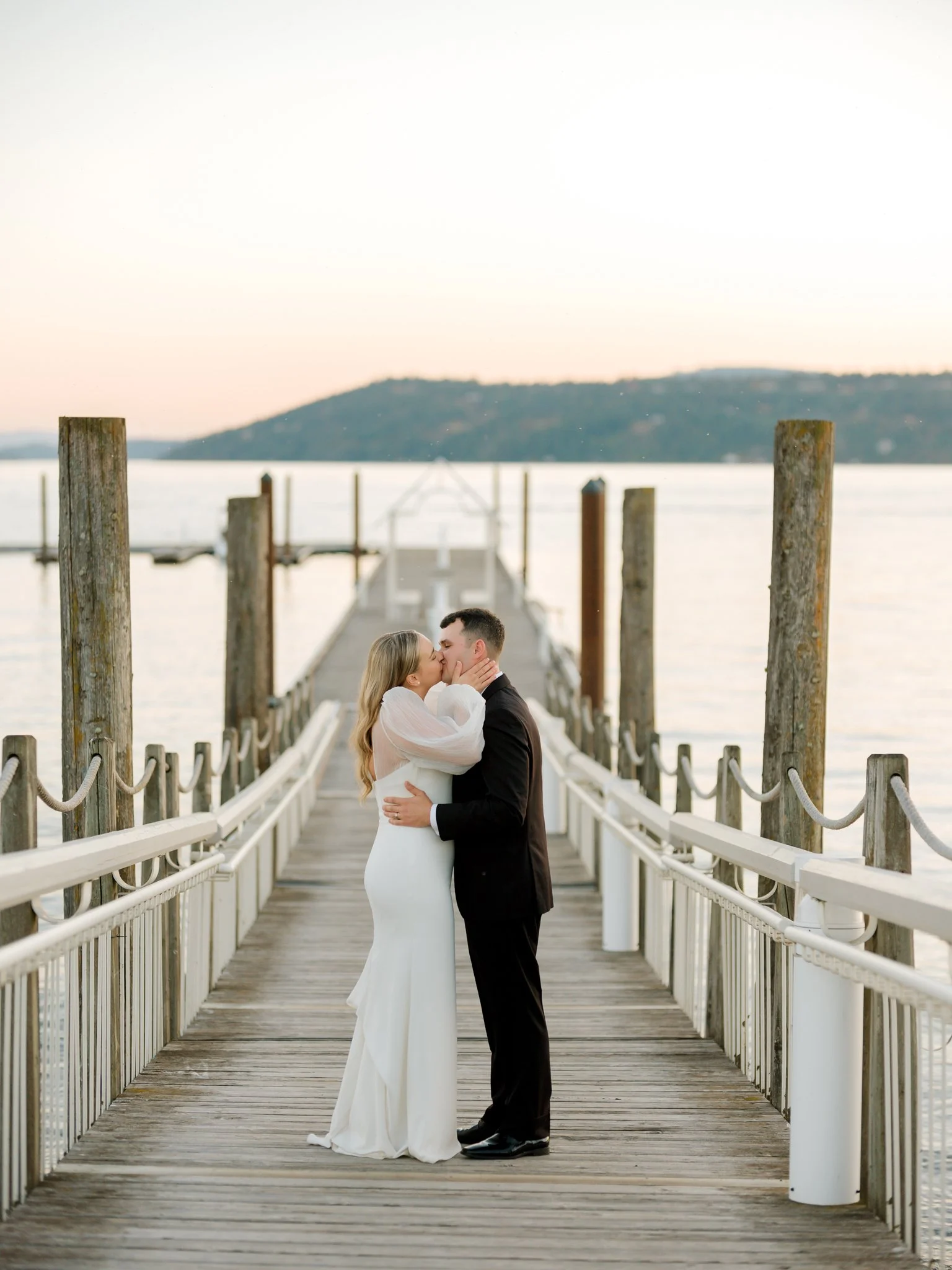 A couple in wedding attire sharing a kiss on a wooden dock by the water at sunset at the Hagadone Event Center in Coeur d'Alene, Idaho.