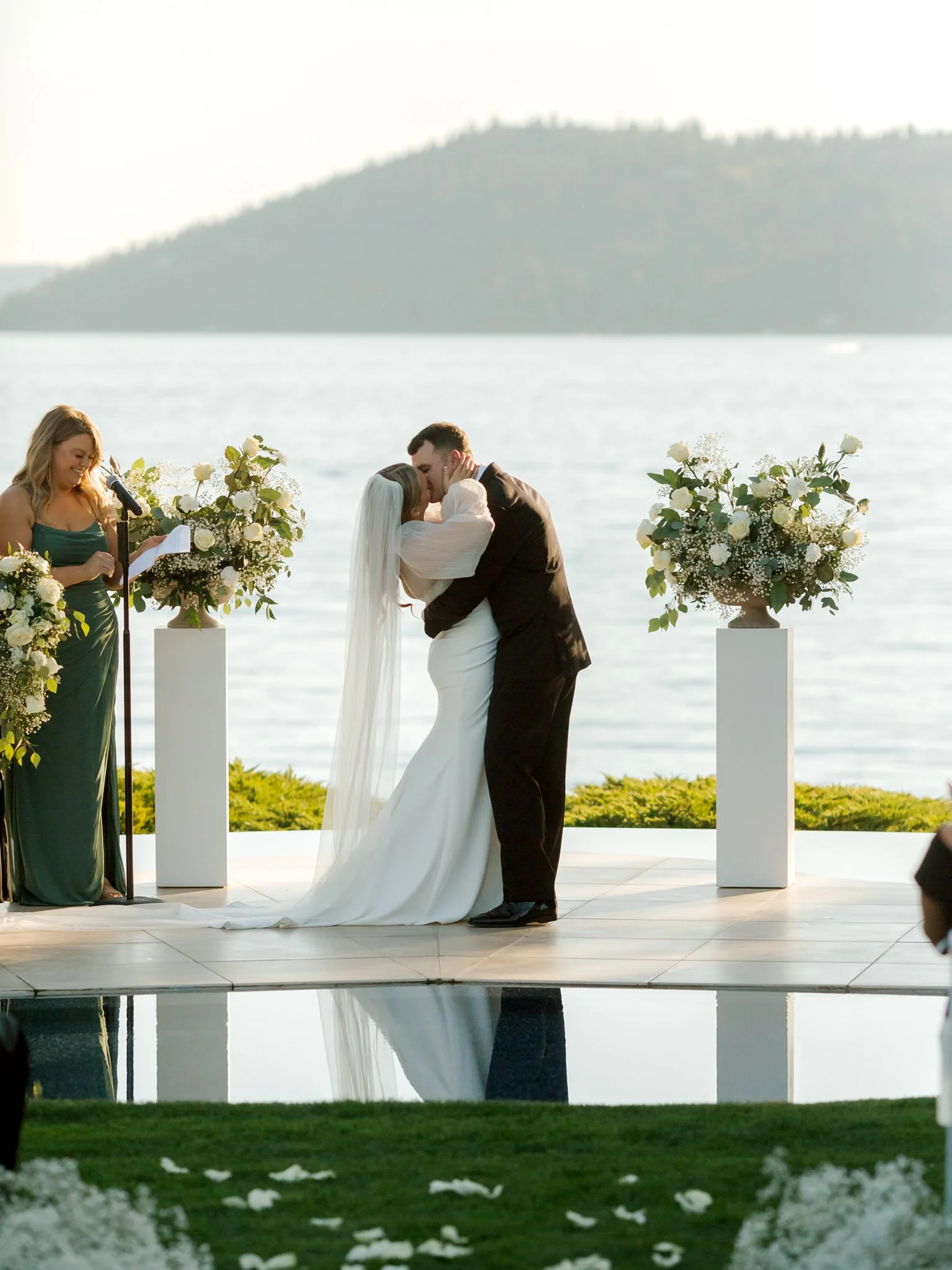 Bride and groom sharing their first kiss with Lake Coeur d’Alene in the background at the Hagadone Event Center ceremony.