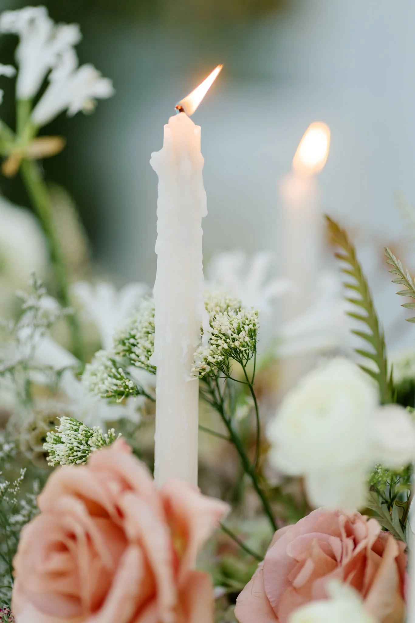 A close-up of a white birthday candle with a flaming wick, surrounded by white flowers and pink roses at Greenhouse on Harvard near Spokane, Washington
