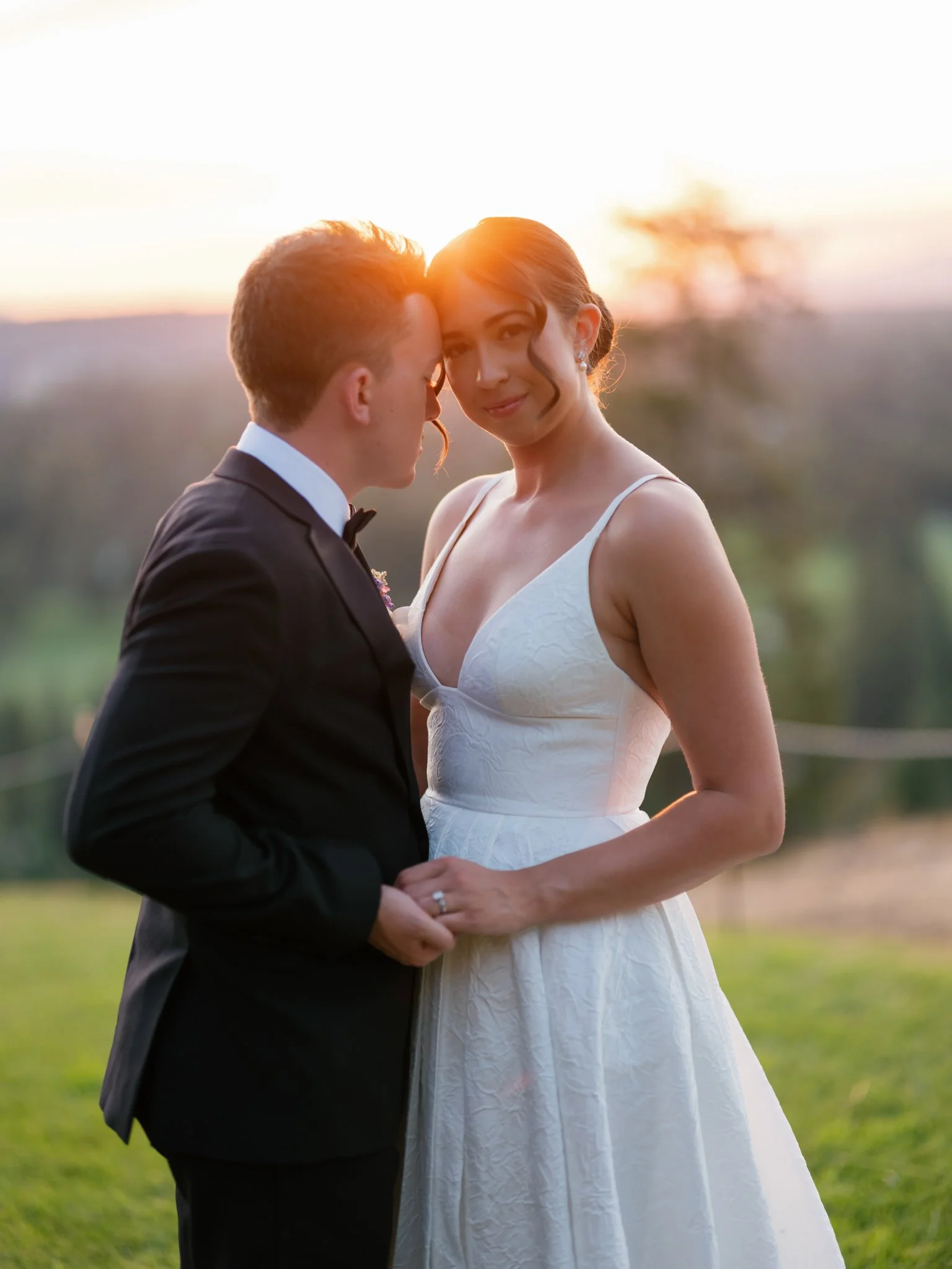 A bride and groom embrace outdoors during sunset, with the bride in a white wedding gown and the groom in a black suit and bowtie at Elk Point wedding in Coeur d’Alene.