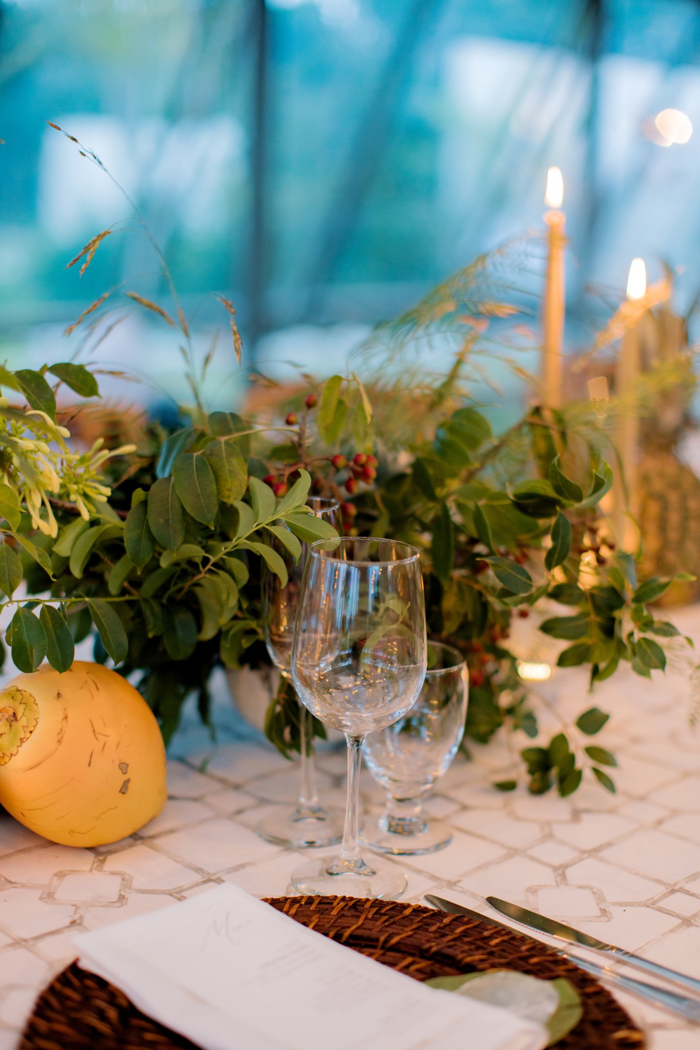 Elegant table setting with empty wine glasses, green foliage centerpiece, candles, and a white tablecloth at The Other Side Hotel during their destination wedding in Eleuthera, Bahamas.