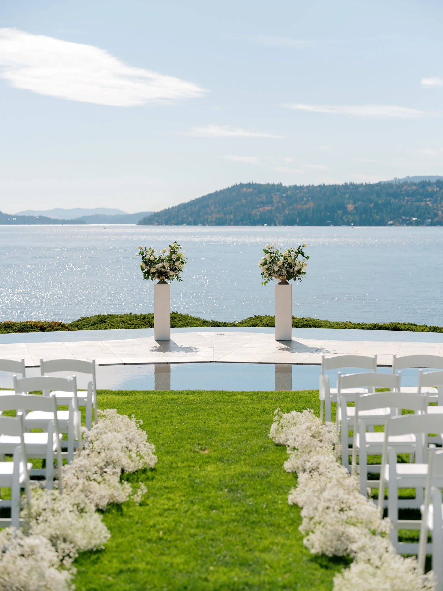Outdoor ceremony setup with white chairs, aisle florals, and panoramic lake views at the Hagadone Event Center in Coeur d’Alene.