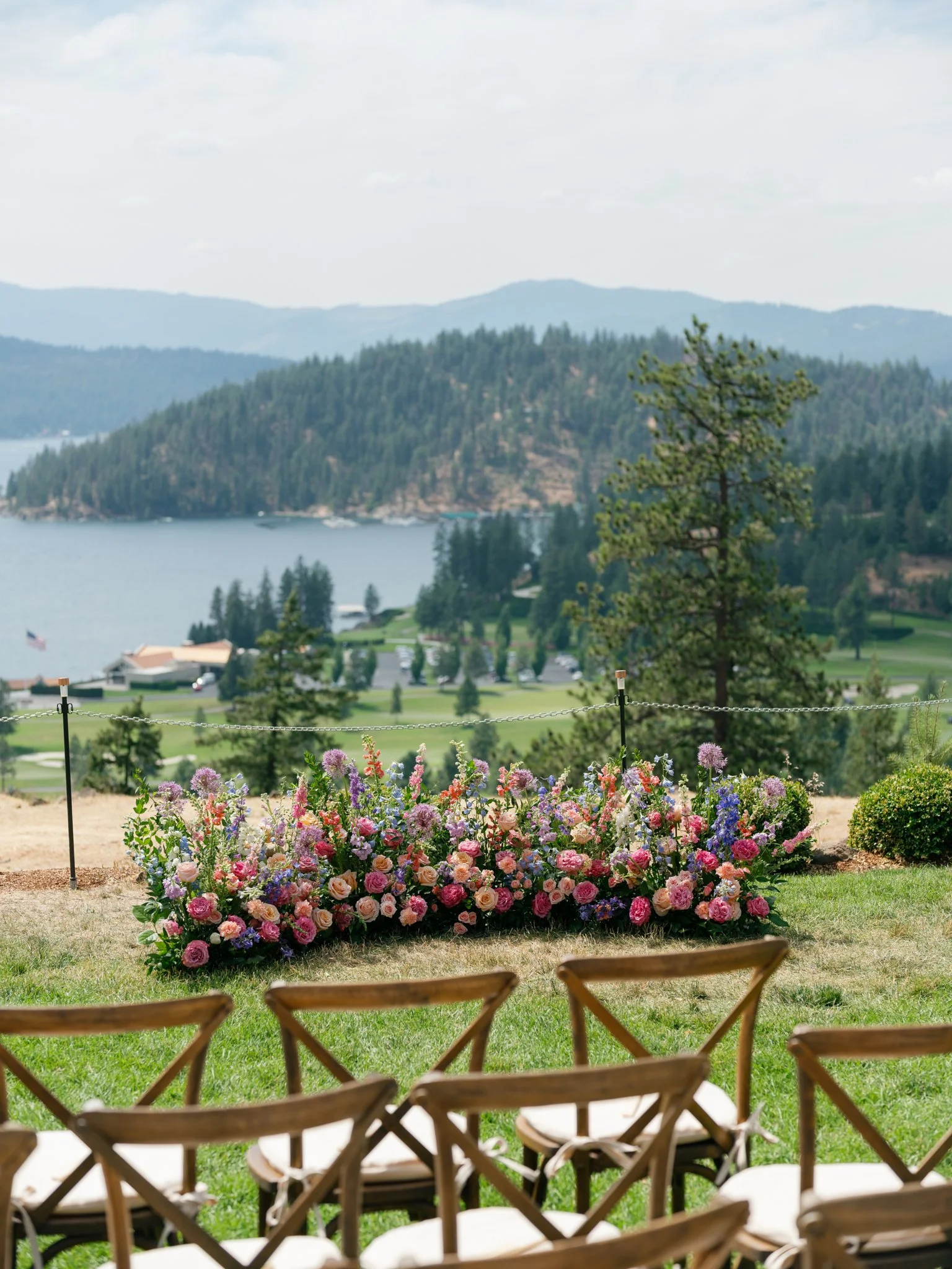 Outdoor wedding setup with a flower arrangement and several chairs facing a scenic lake and forested hills at Elk Point wedding above Lake Coeur d’Alene.