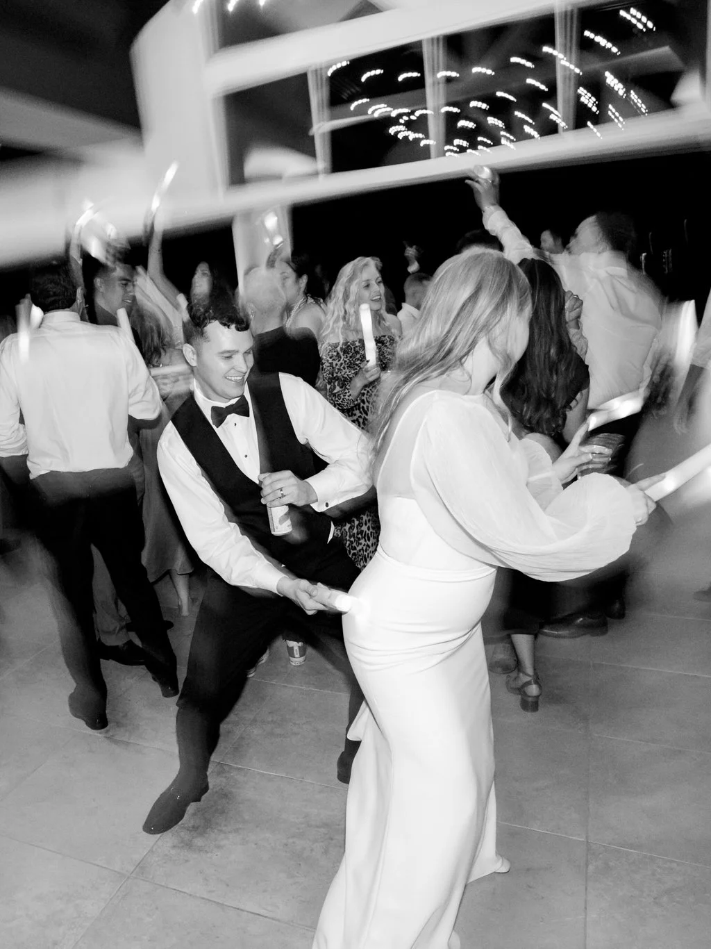 Couple playing tug of war at a celebration, people dancing and laughing in background.