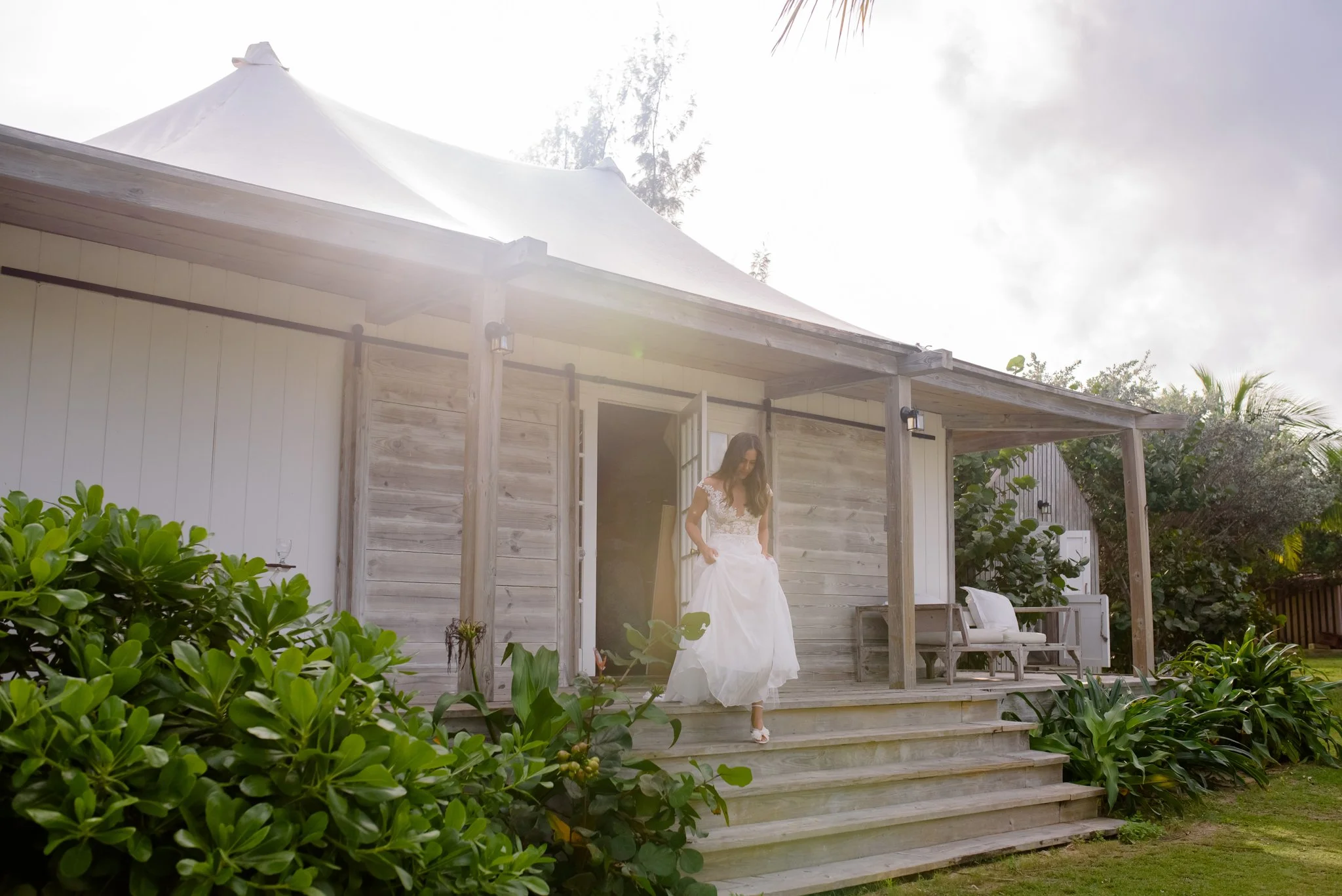 A woman in a wedding dress stepping down from a wooden porch of a house with greenery around at The Other Side Hotel Eleuthera during a luxury Bahamas destination wedding.