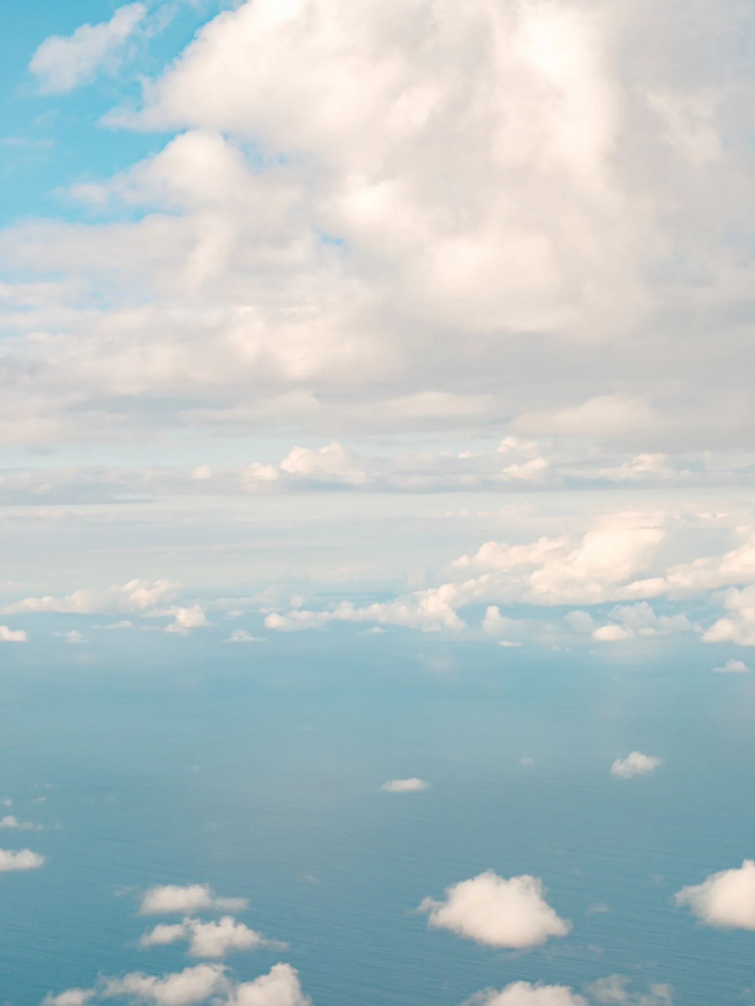 View of the sky from above with scattered clouds over the ocean.