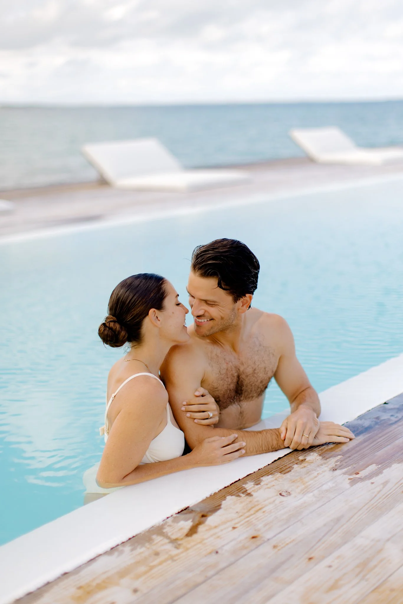 A couple enjoying a tender moment together in a pool by the seaside, smiling and embracing each other, during their Bahamas destination wedding.