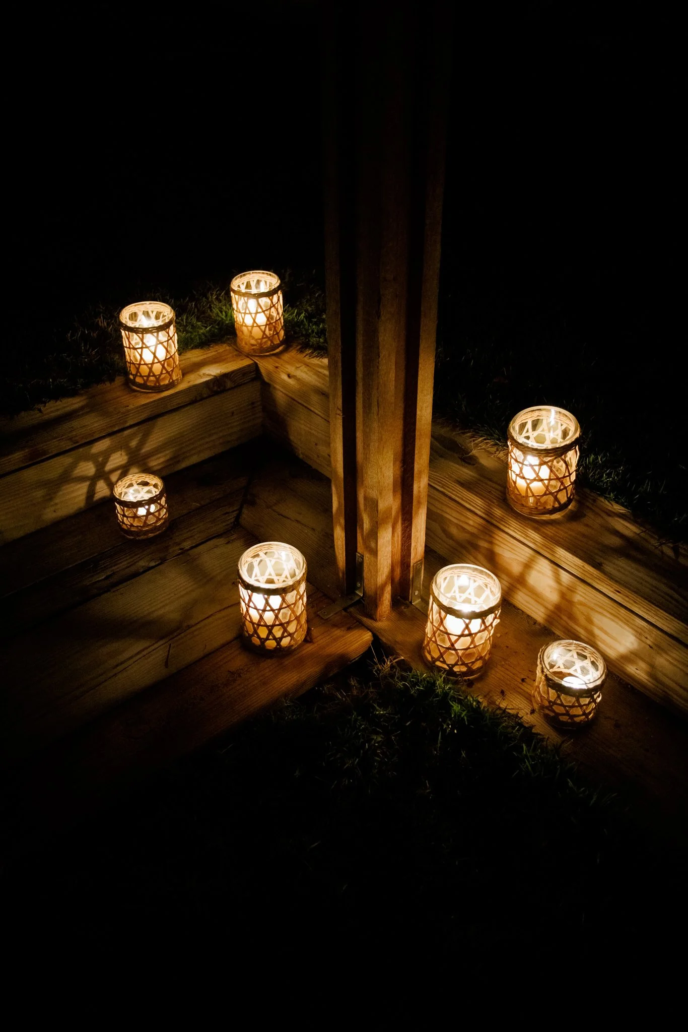 Candles in decorative holders placed along a wooden staircase at night.
