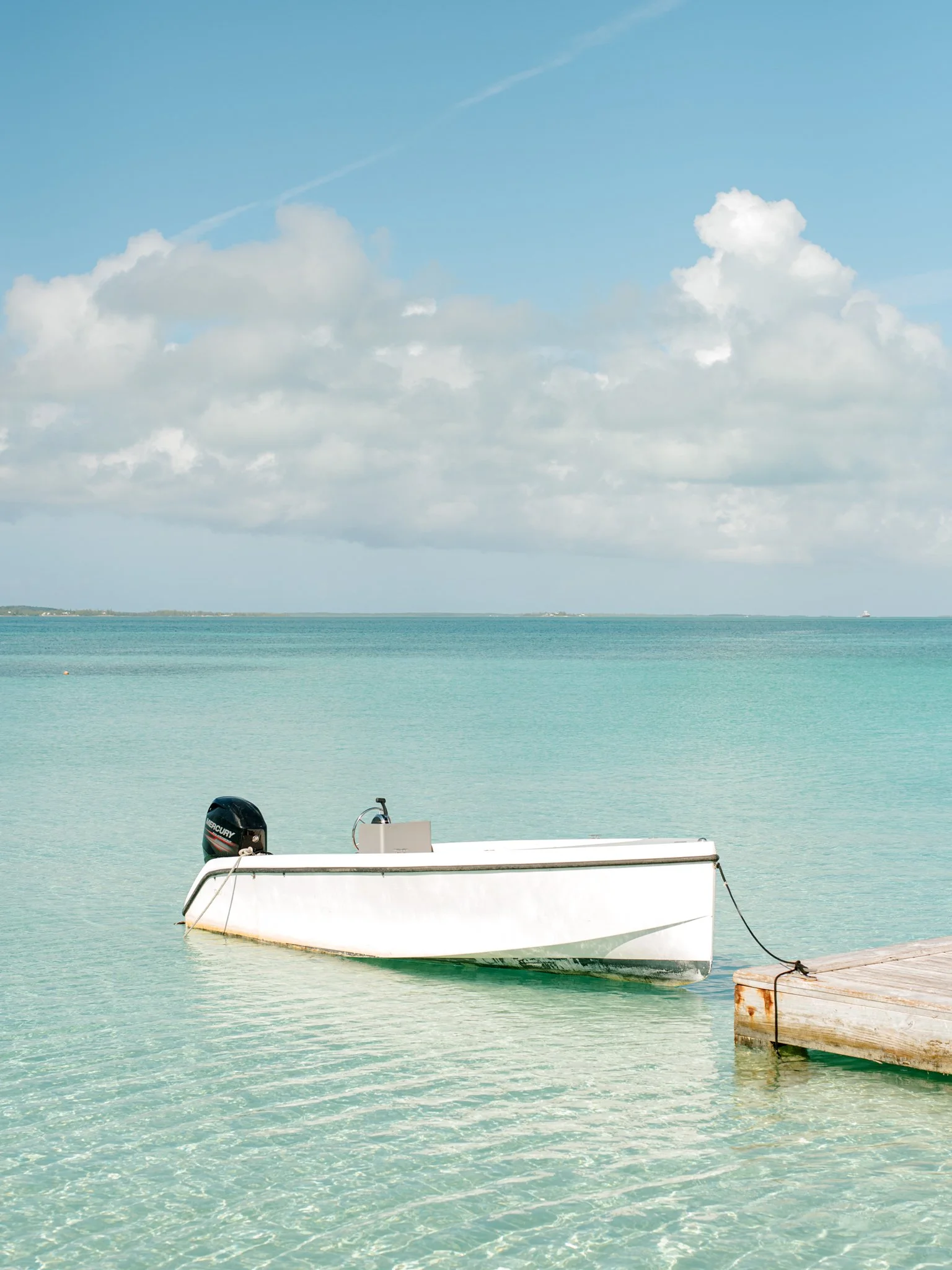 A white boat tied to a wooden dock on clear, turquoise water with a cloudy sky overhead at The Other Side Hotel during their destination wedding in Eleuthera, Bahamas.
