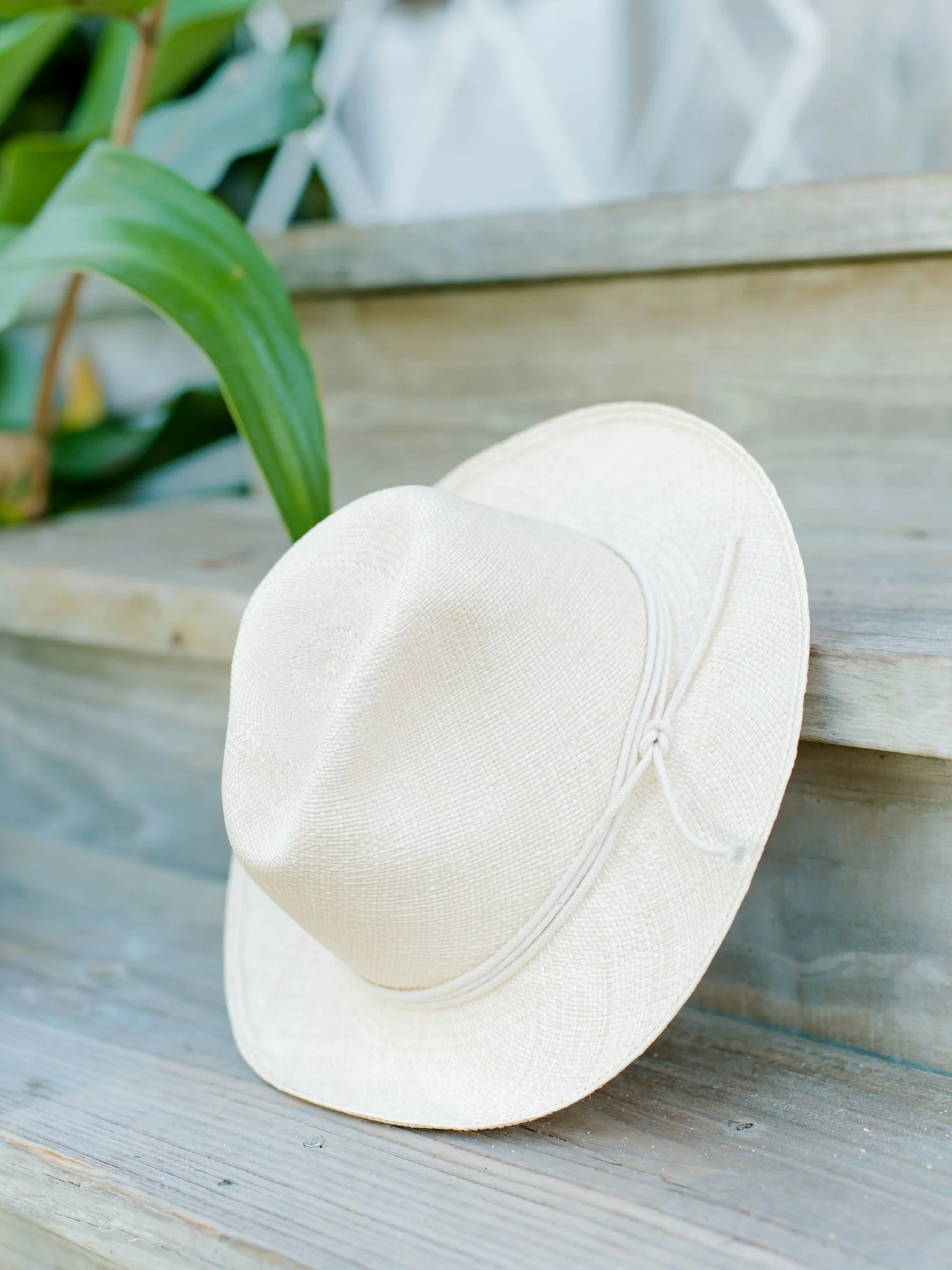 A white straw sun hat with a chin strap resting on wooden steps outdoors at The Other Side Hotel during their destination wedding in Eleuthera, Bahamas.