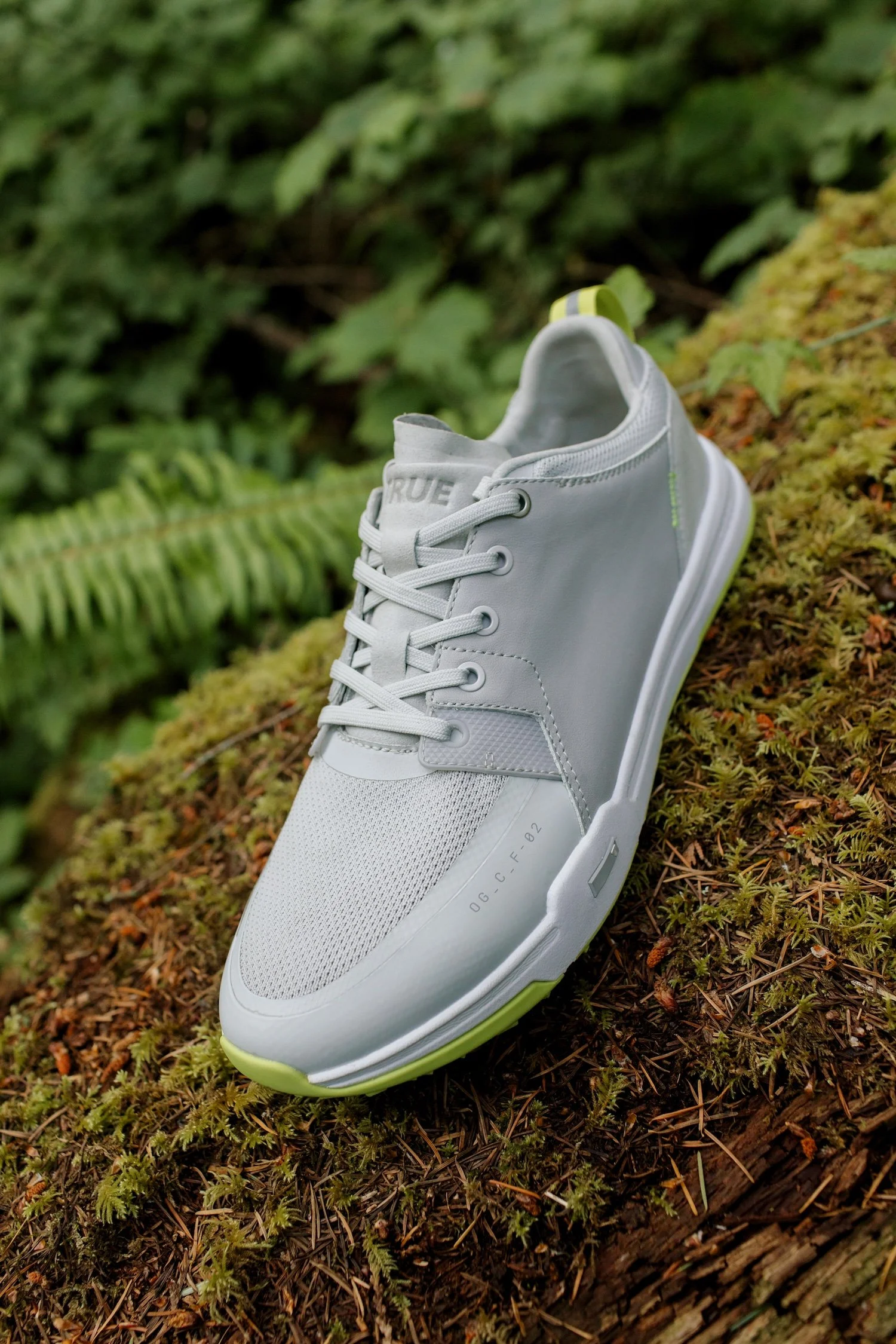 A white athletic shoe with green accents resting on moss and surrounded by lush green foliage.