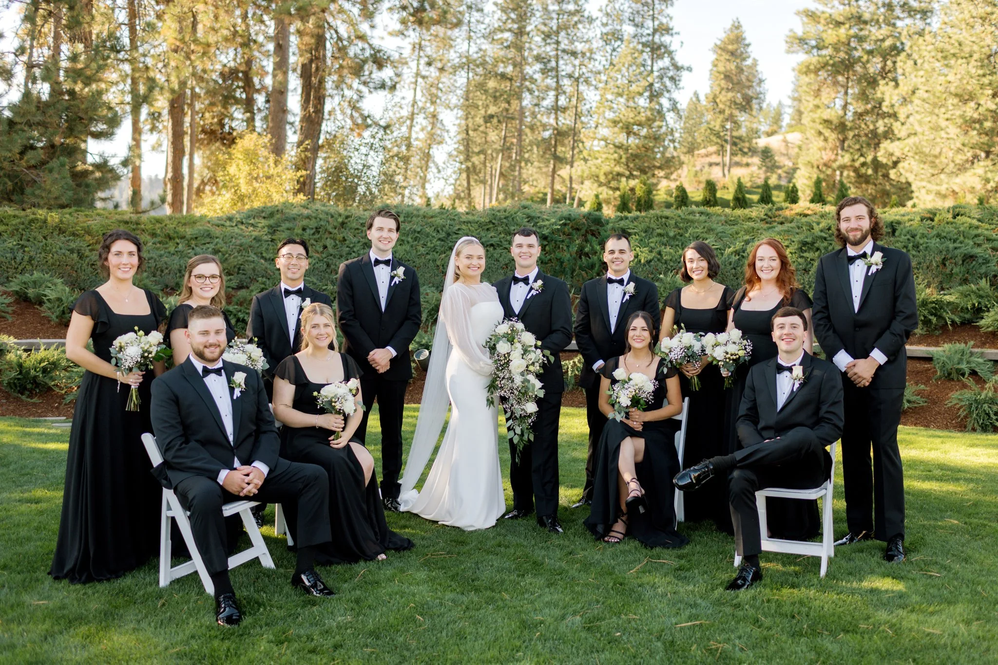 Full wedding party portrait with bridesmaids in black dresses and groomsmen in tuxedos at the Hagadone Event Center in Coeur d’Alene.