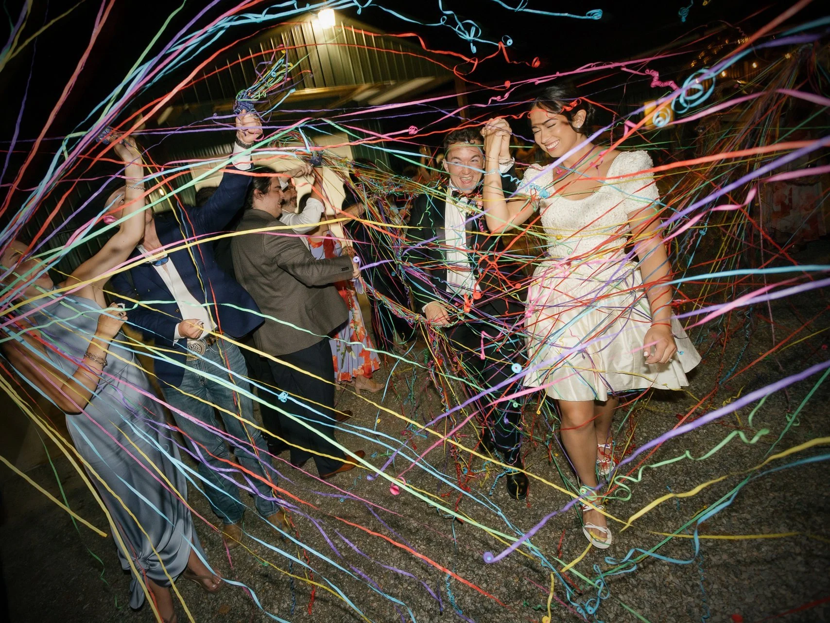 People celebrating at a party with colorful streamers and ribbons, joyful expressions, dancing and holding hands.