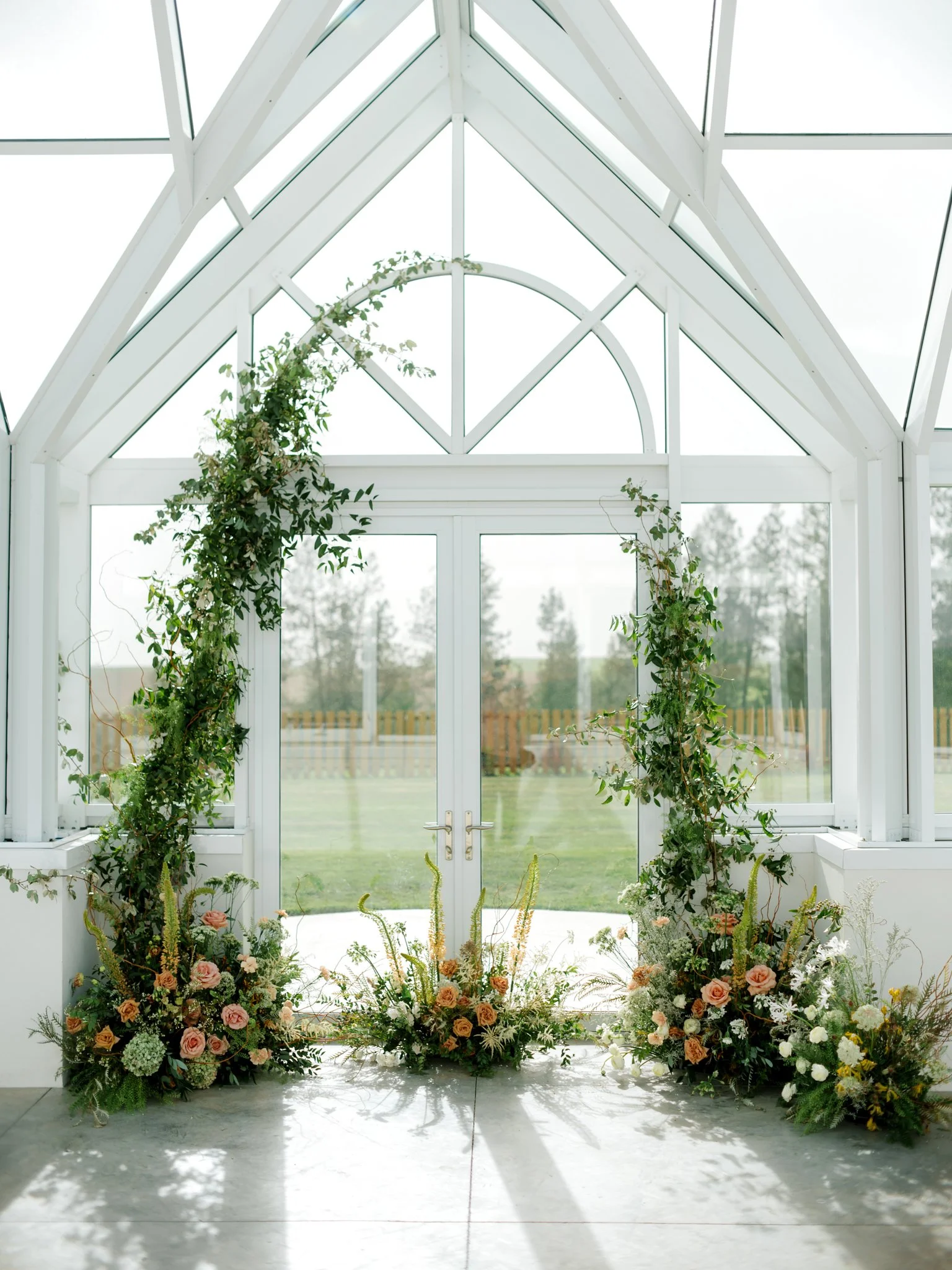 Floral arrangements and greenery decorating the inside of a glass and white framework structure, possibly for a wedding or event at Greenhouse on Harvard near Spokane, Washington.