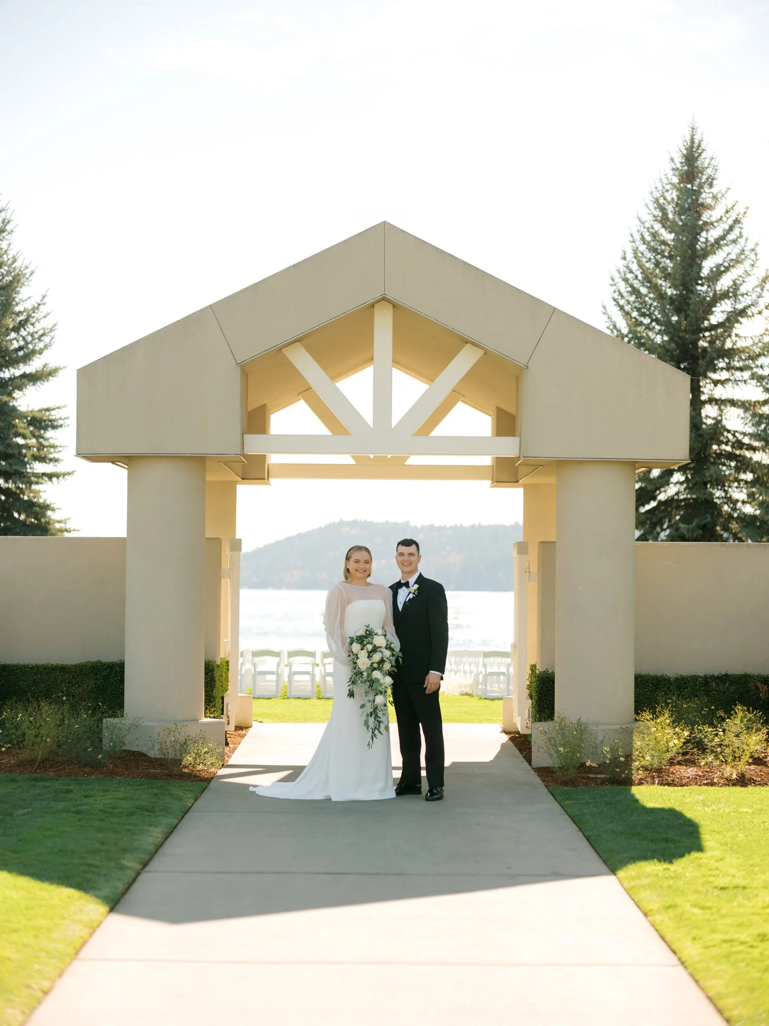 Bride and groom standing beneath the architectural archway overlooking Lake Coeur d’Alene at the Hagadone Event Center.