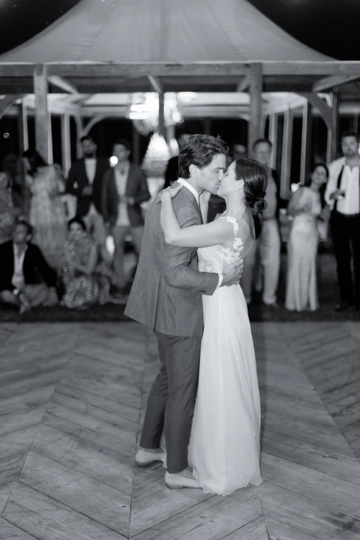 A black and white photograph of a bride and groom kissing during their wedding reception, with wedding guests in the background at The Other Side Hotel during their destination wedding in Eleuthera, Bahamas.