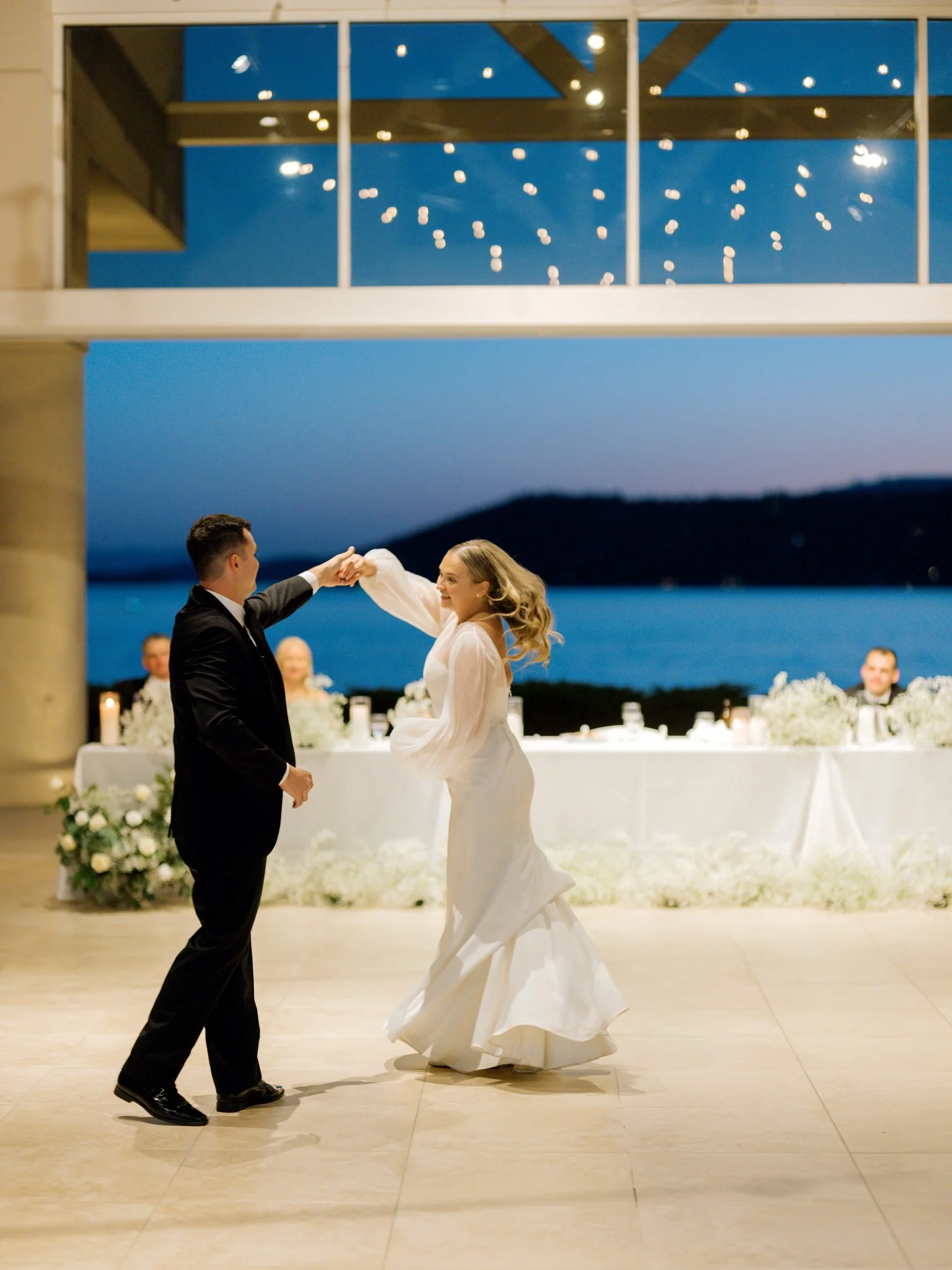 A bride and groom dancing at their wedding reception with a lake and mountains in the background, during the evening at the Hagadone Event Center in Coeur d'Alene, Idaho.
