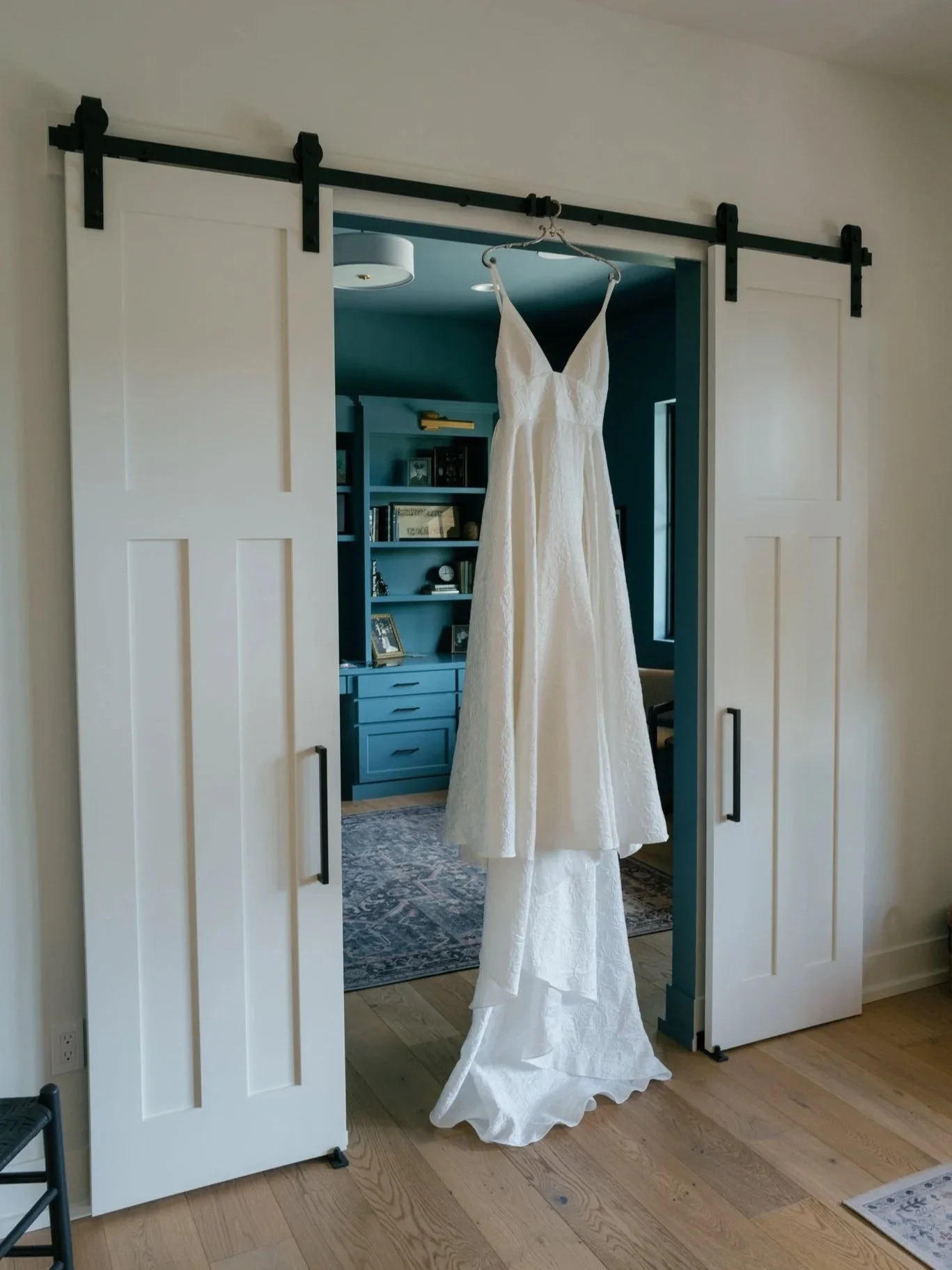 A white wedding dress hanging on a hanger in front of a set of sliding barn doors.