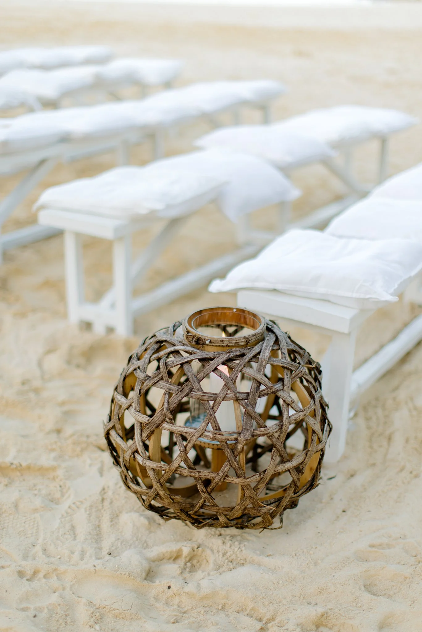 Beach scene with white lounge chairs and pillow, wooden lantern on the sand.