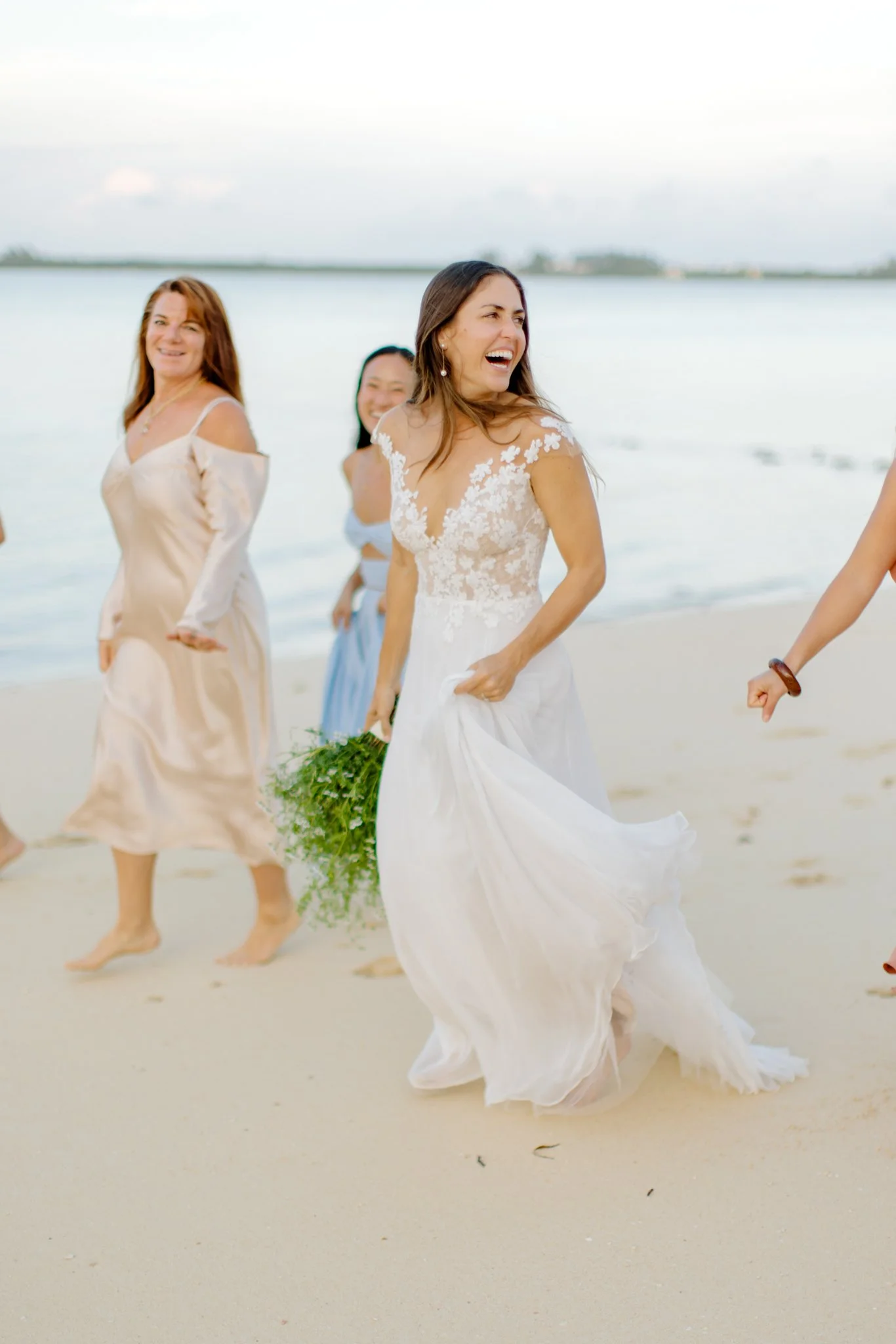 A group of women in dresses walking on a beach, smiling and laughing, with the ocean in the background at The Other Side Hotel Eleuthera during a luxury Bahamas destination wedding.