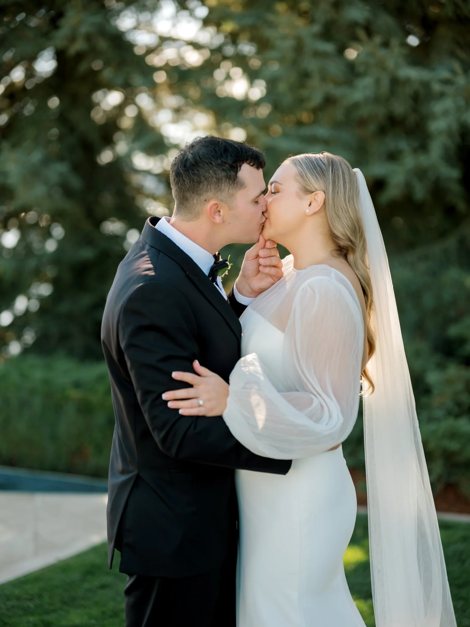 Bride and groom sharing a kiss during outdoor portraits surrounded by evergreens at the Hagadone Event Center in Coeur d’Alene.